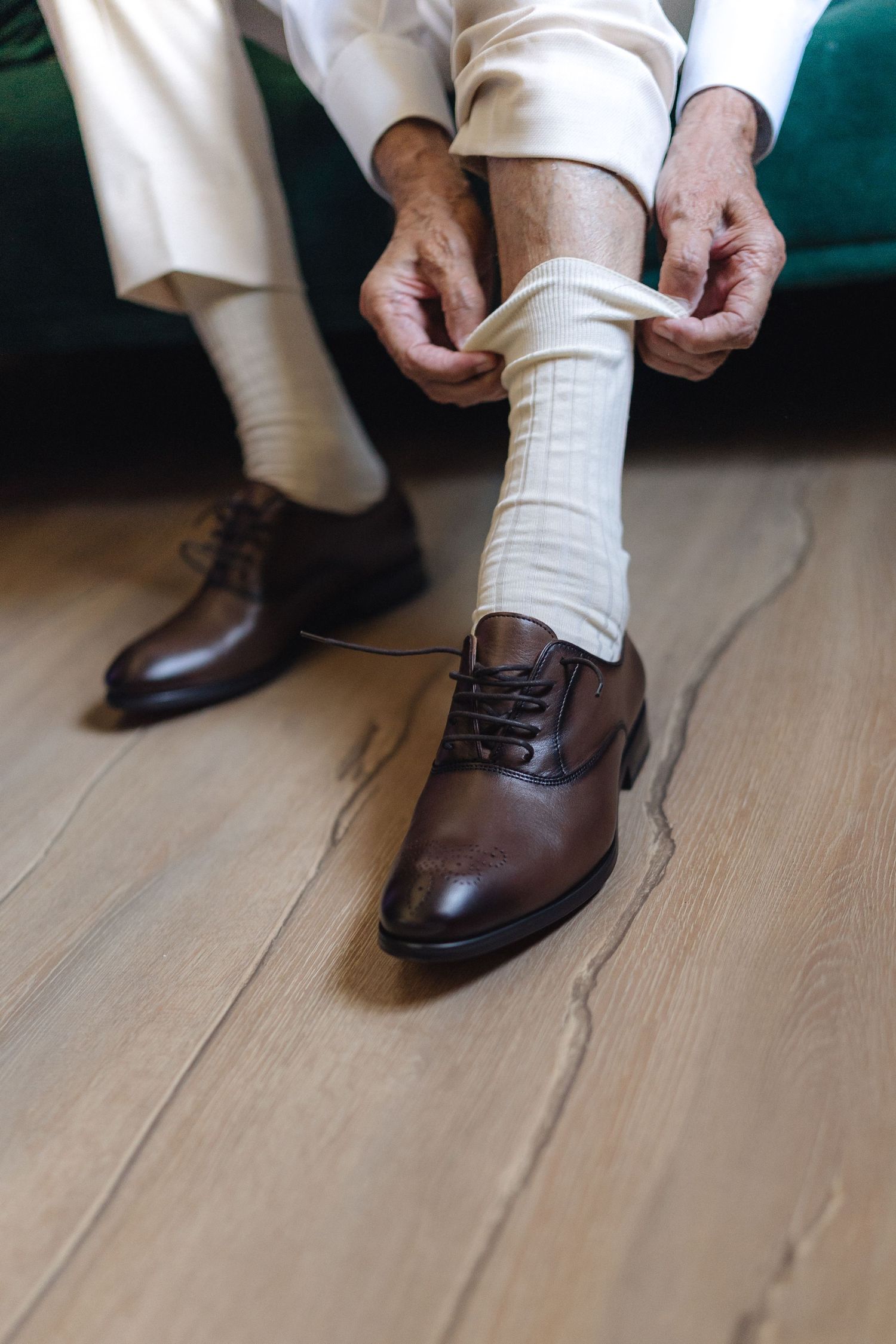Close-up sequence showing someone putting on brown dress shoes and white socks on a wooden floor.