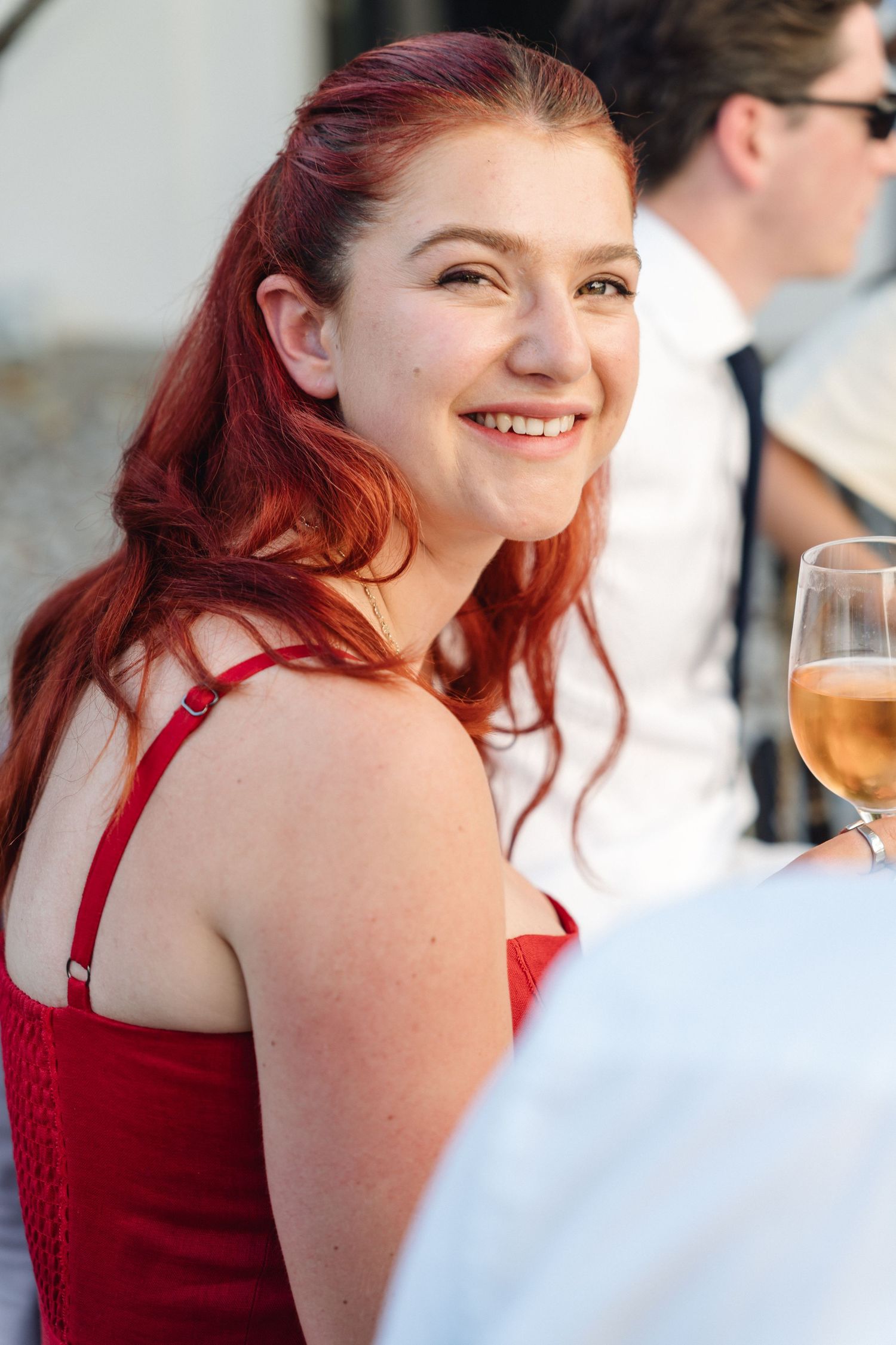 A guest in a red dress enjoys wine at an outdoor reception.