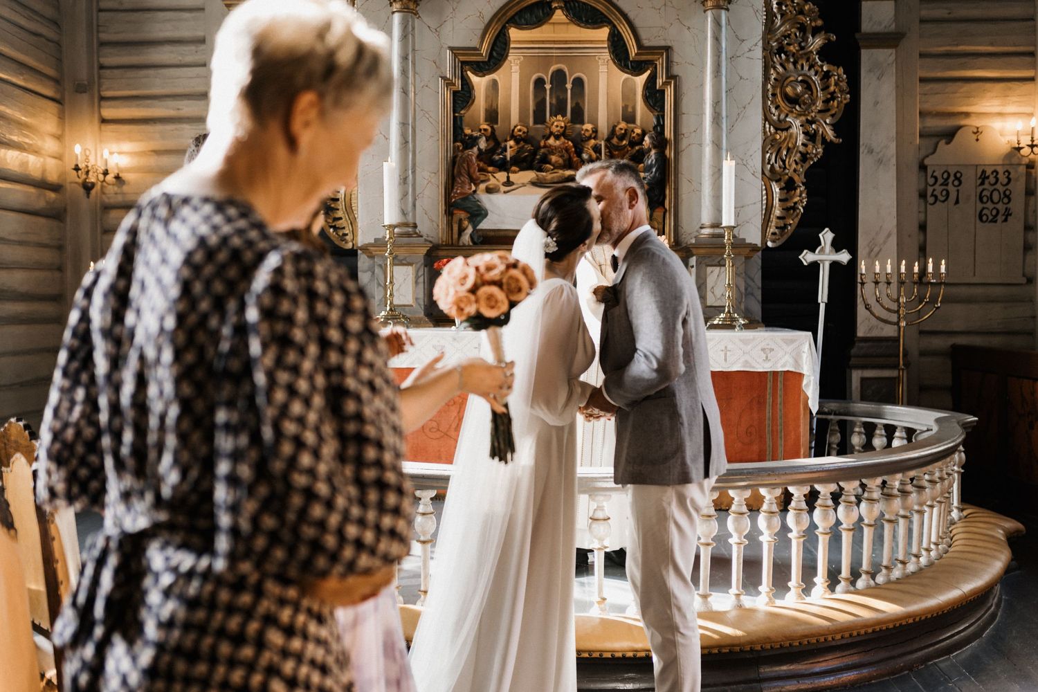 Bride and groom share a kiss at the altar of an ornate church during their wedding ceremony.