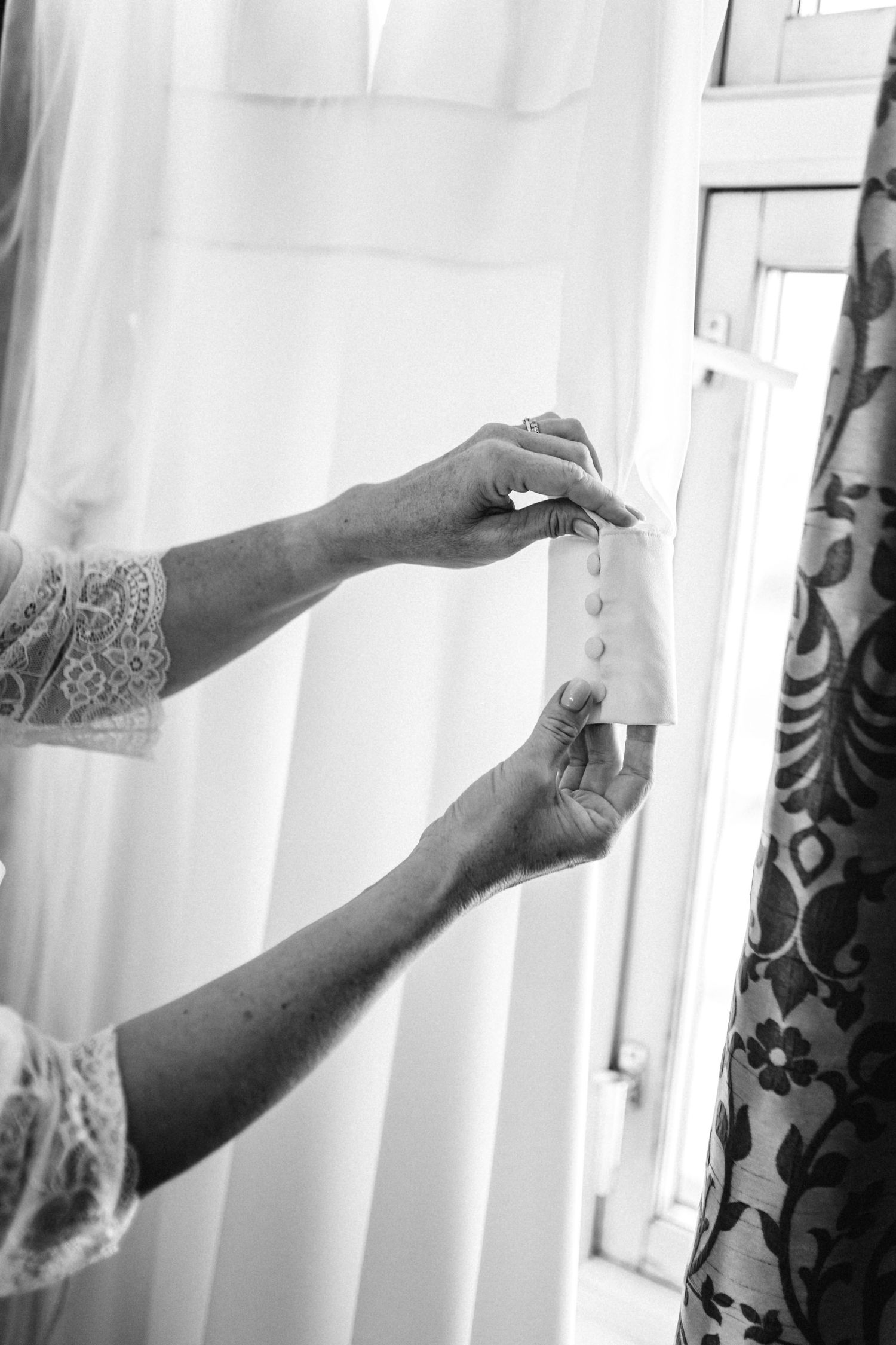Close-up of hands adjusting white curtains in natural light.
