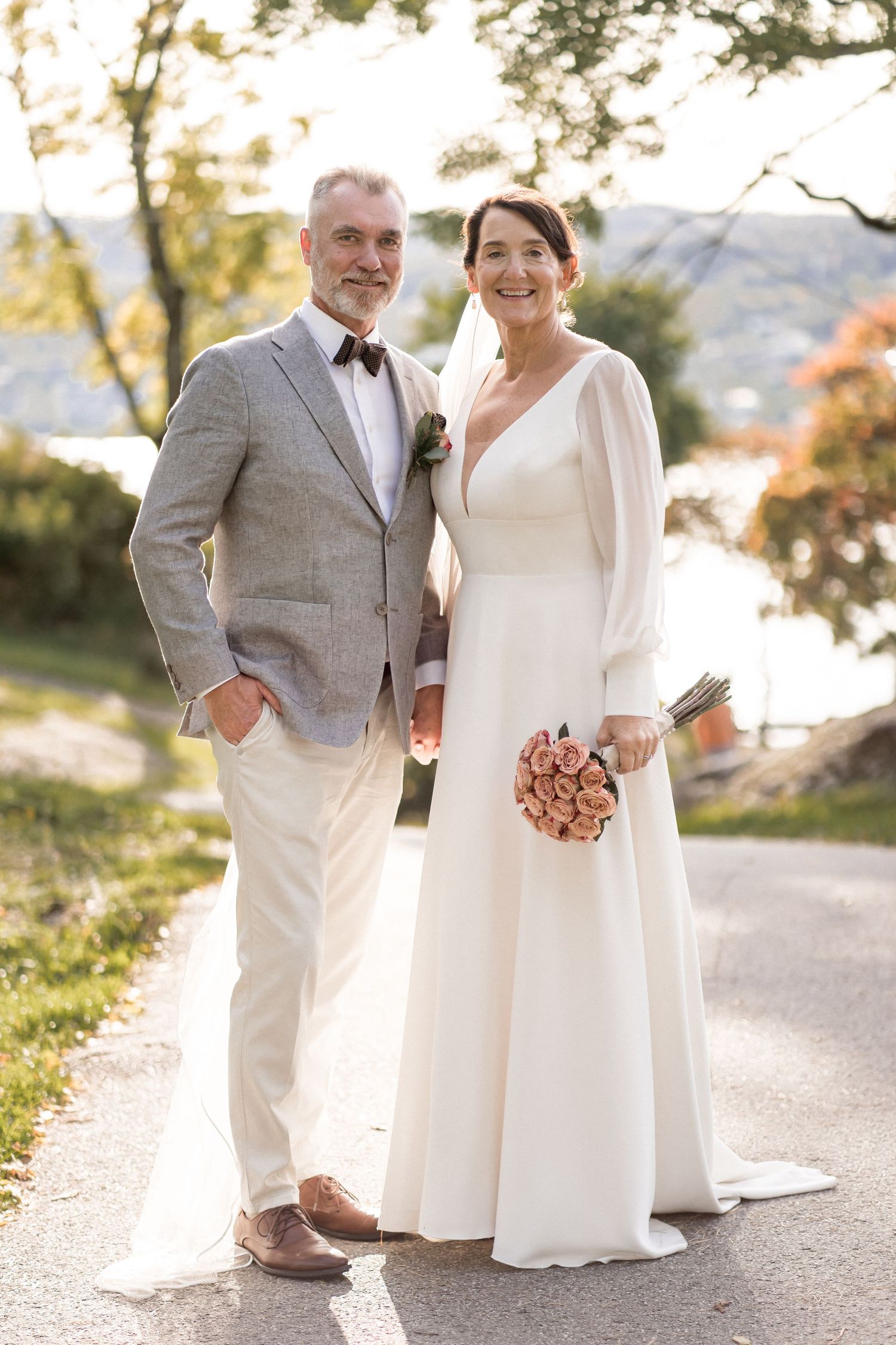 Romantic outdoor wedding photos on a path with autumn trees in the background.