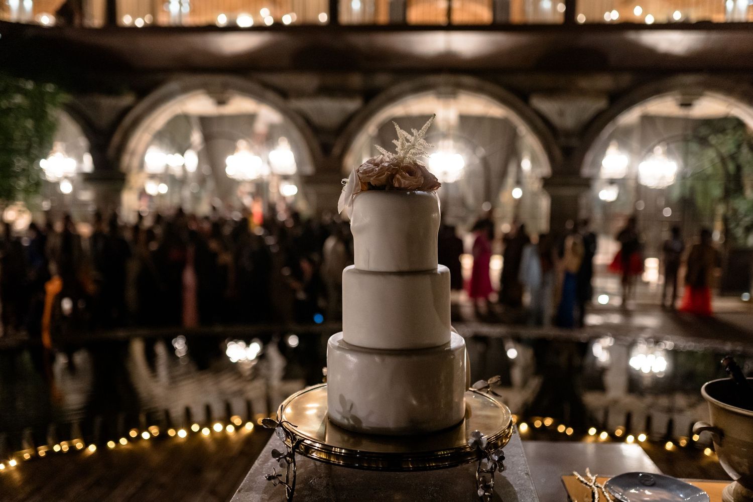 Elegant three-tiered white wedding cake displayed against illuminated stone arches at night.