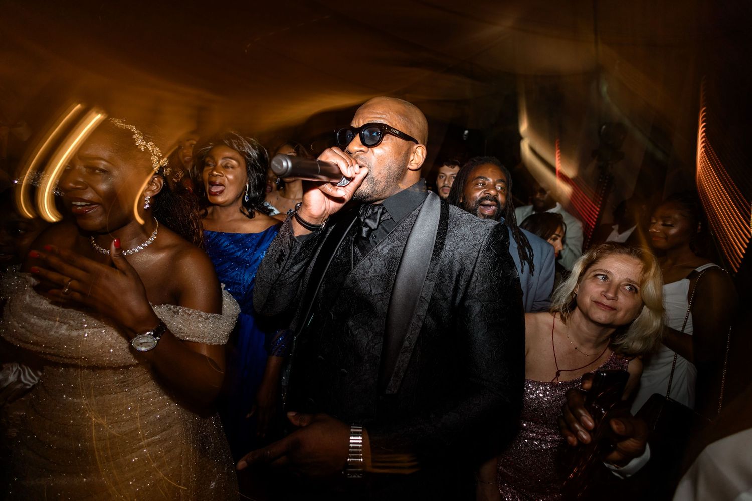 Wedding guests dancing and celebrating on a dimly lit dance floor.