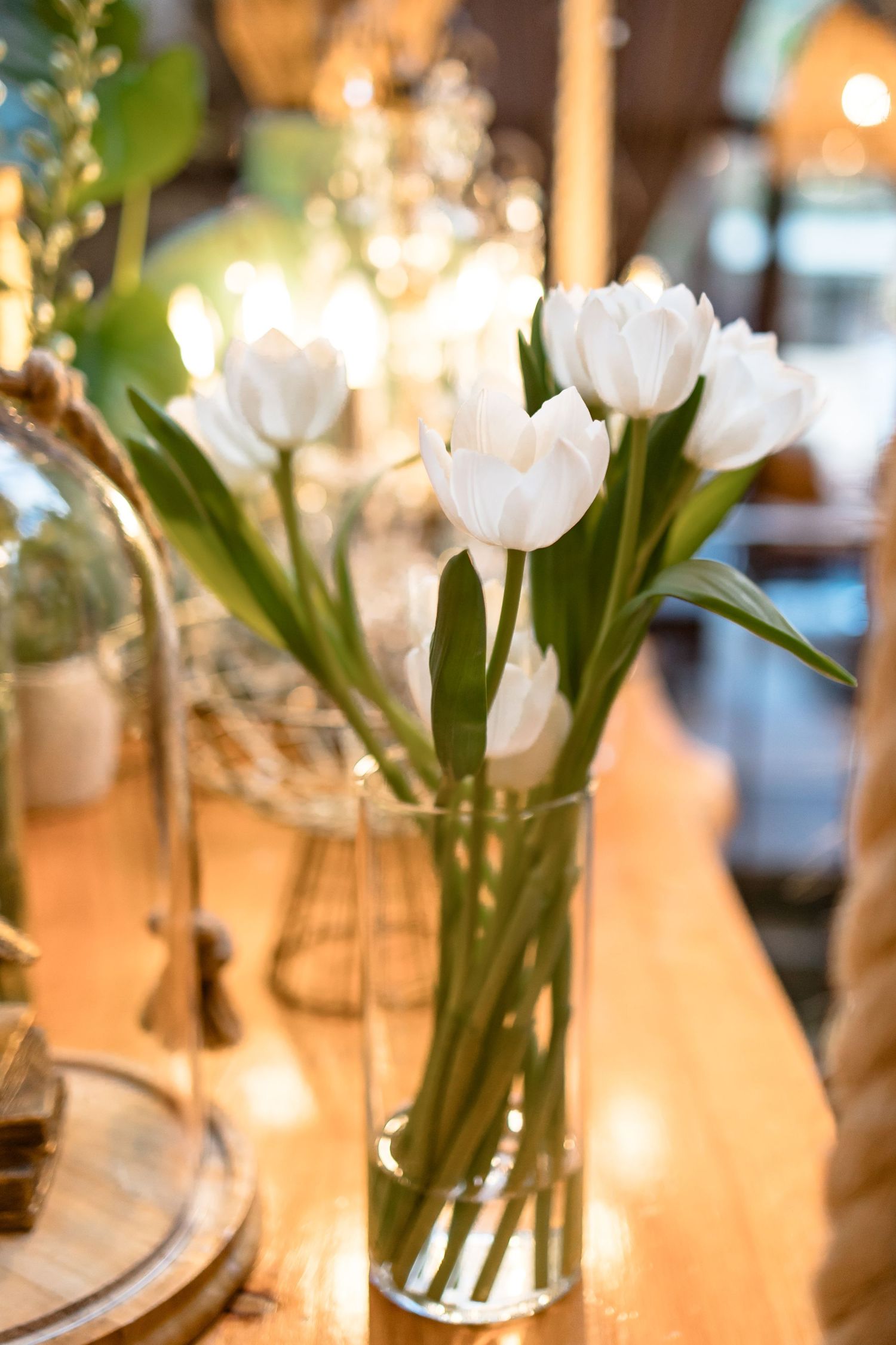 White tulips in glass vases arranged as elegant wedding centerpieces with warm ambient lighting.