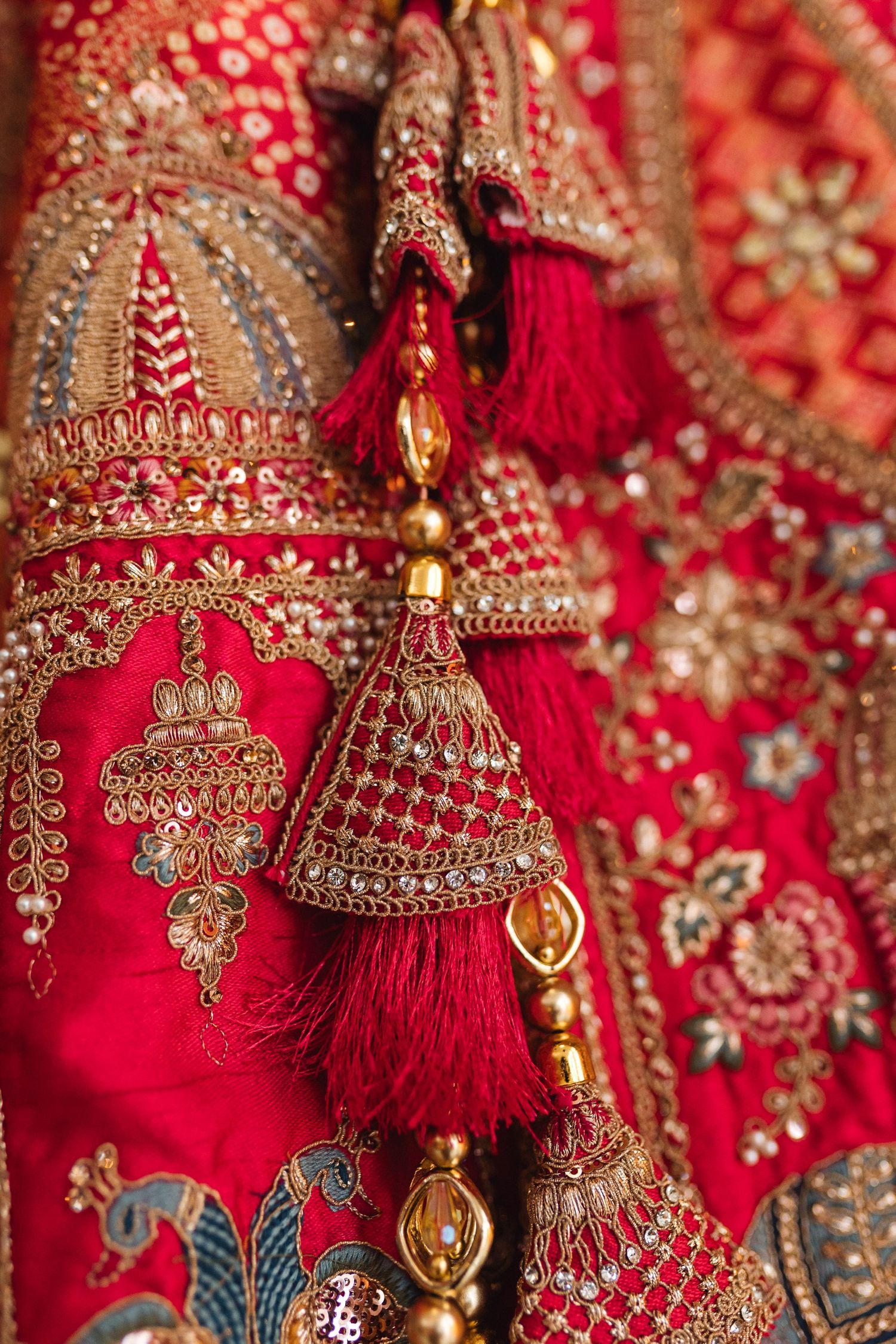 Ornate red and gold embroidered Indian wedding attire with decorative tassels and bells.