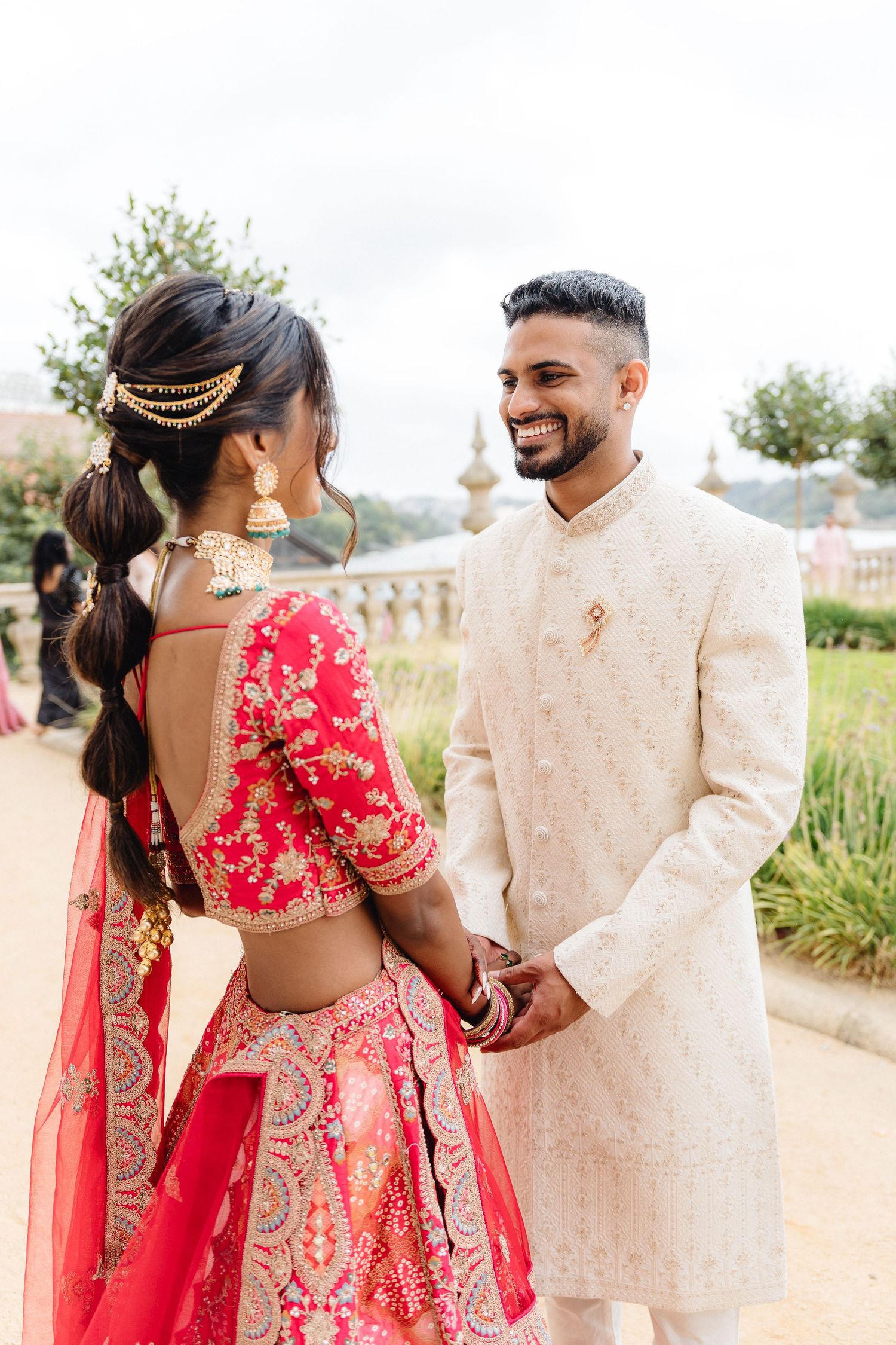 Couple in traditional Indian wedding attire walking together in an outdoor garden setting.
