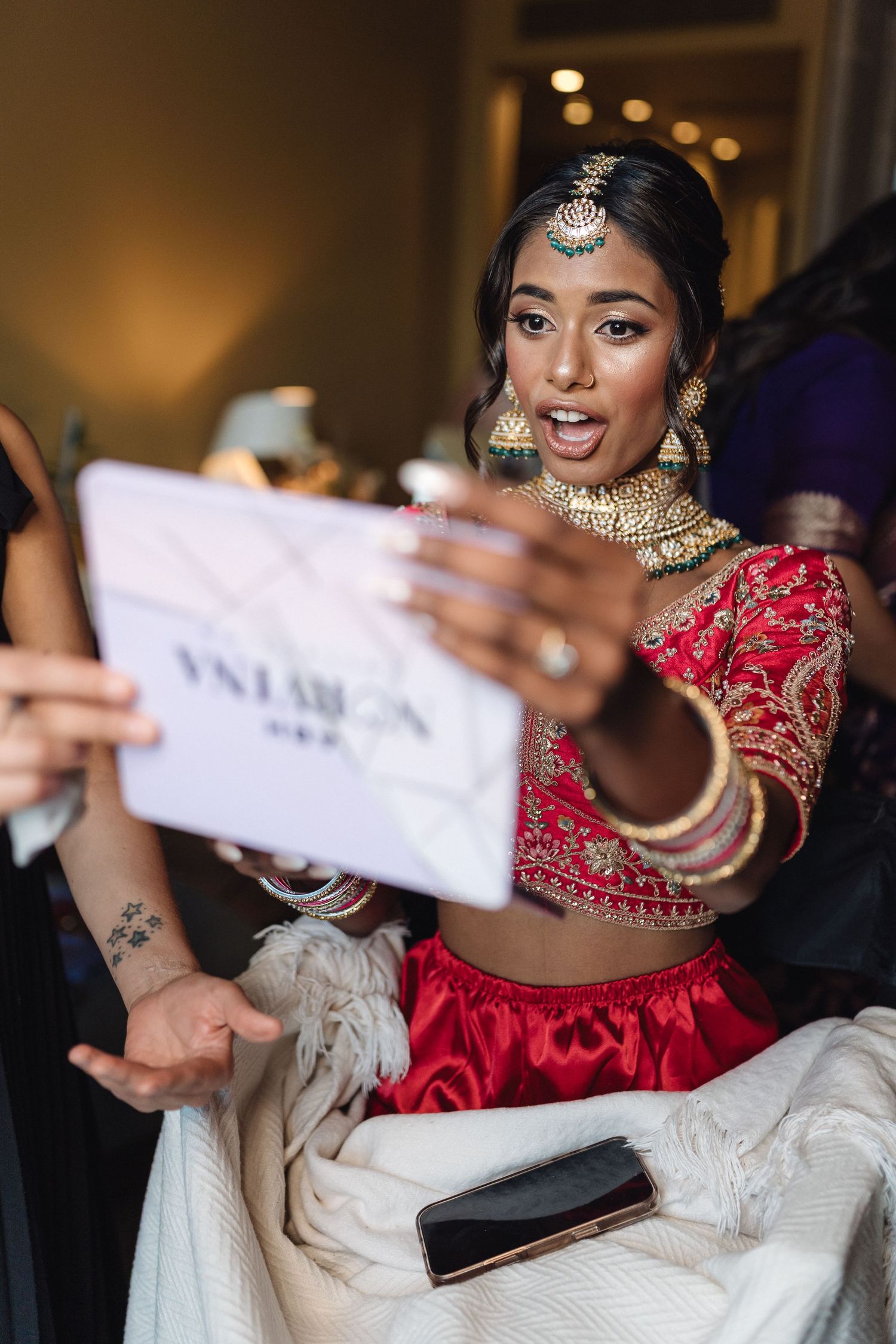 Close-up of traditional Indian bride in red lehenga reading a note during wedding preparations.