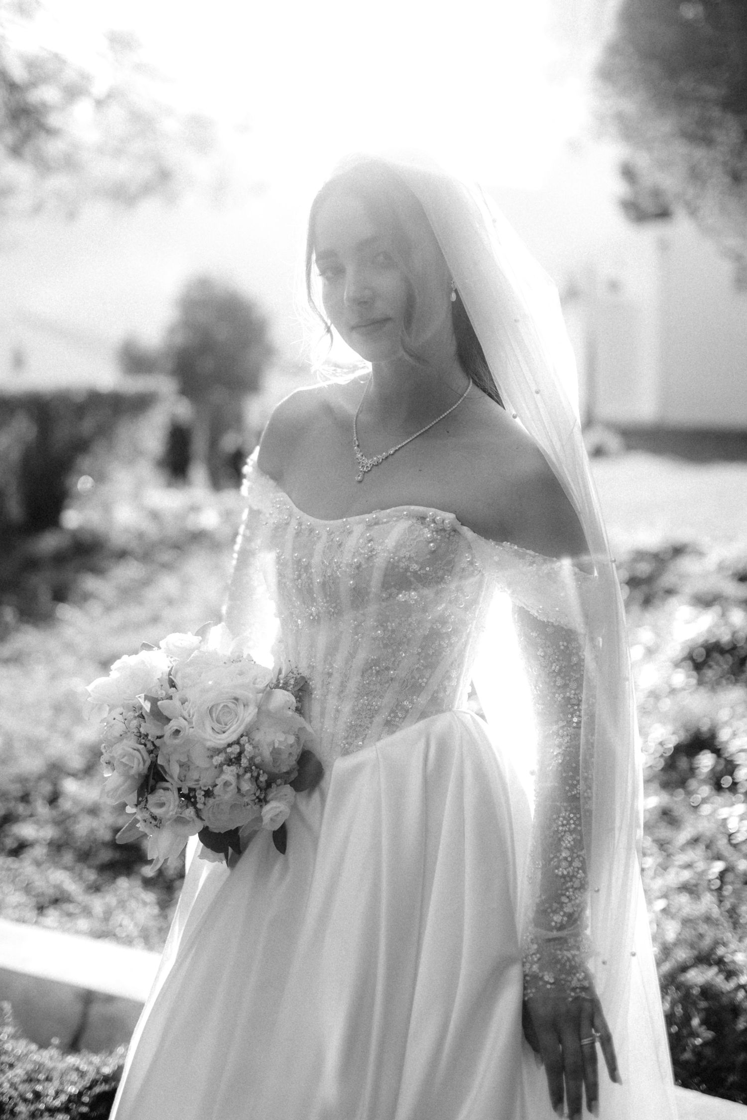 Black and white bridal portrait showing ethereal details of a lace wedding dress and bouquet in soft lighting.