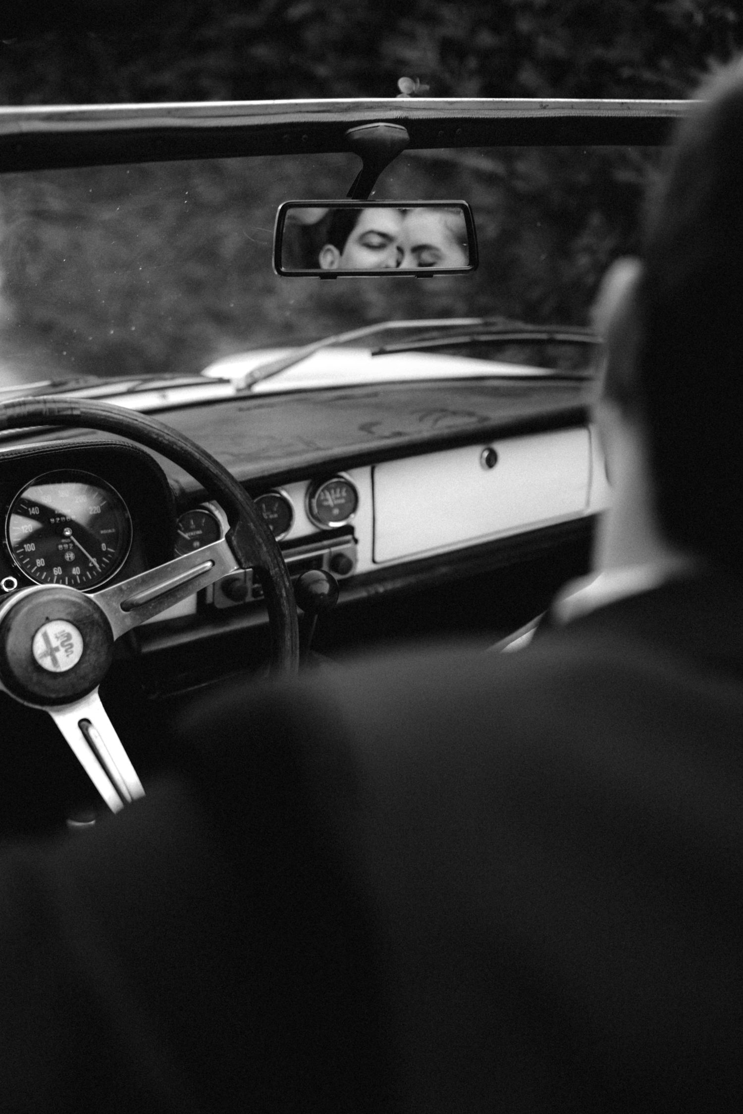 Couple sharing a kiss reflected in the rearview mirror of a classic vintage car.