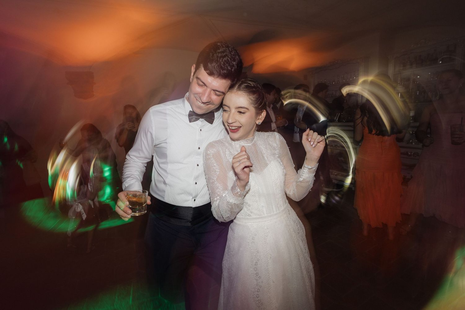 Happy bride and groom dancing together at their wedding reception surrounded by colorful lights.