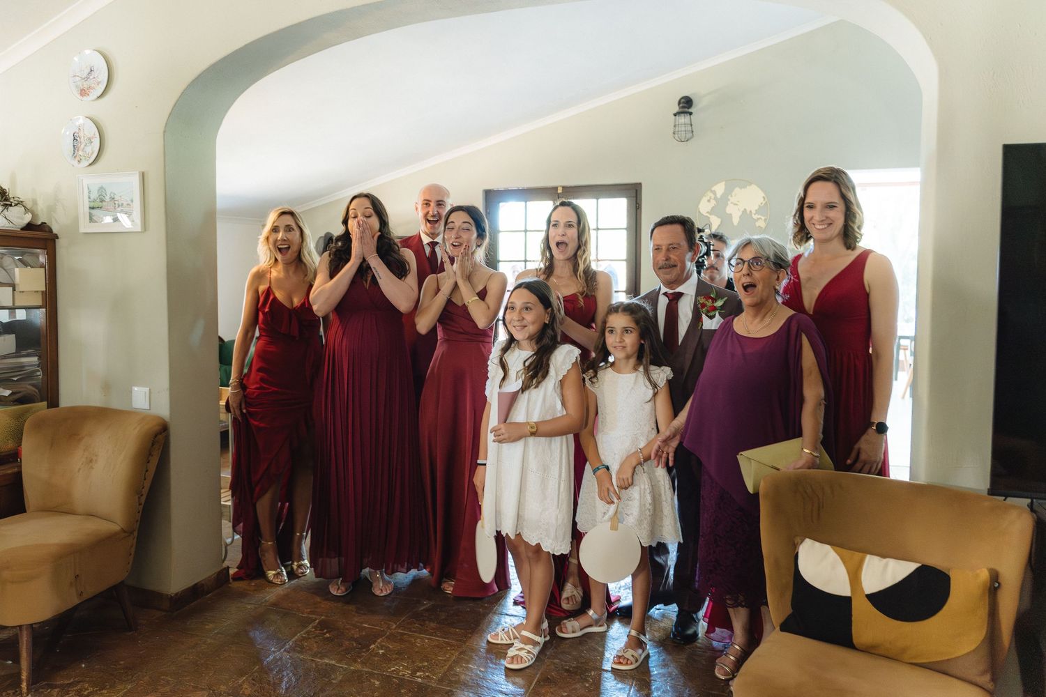 Wedding party group photo with people wearing burgundy and white dresses in an indoor venue.