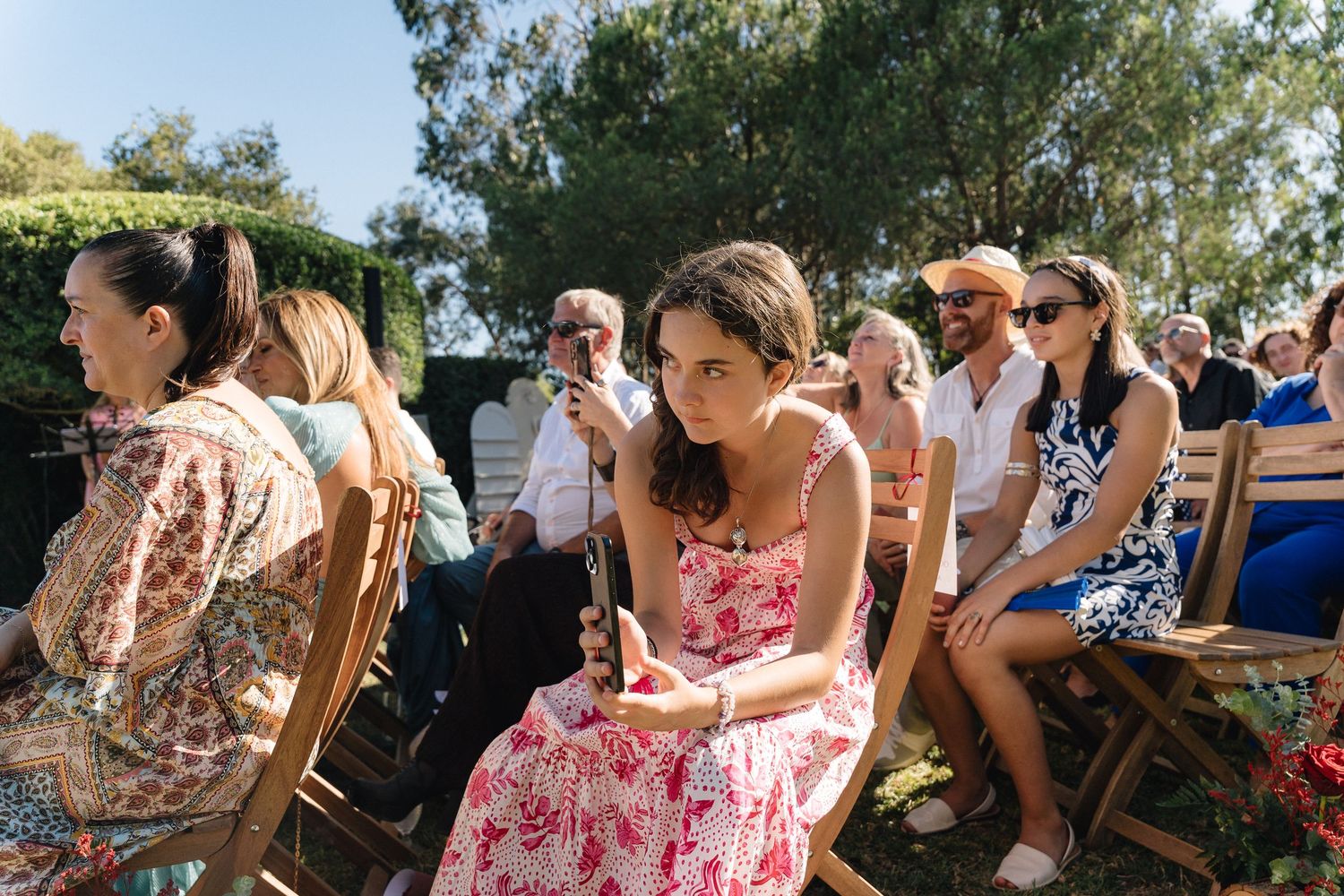 Wedding guests seated on wooden chairs at outdoor ceremony venue.