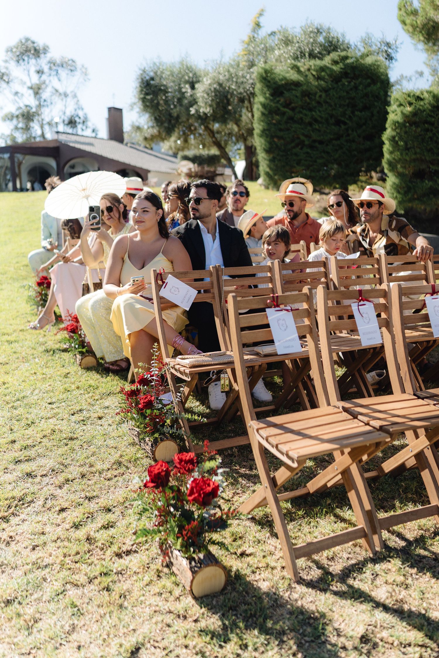 Wooden folding chairs decorated with red roses line hillside outdoor wedding ceremony space.