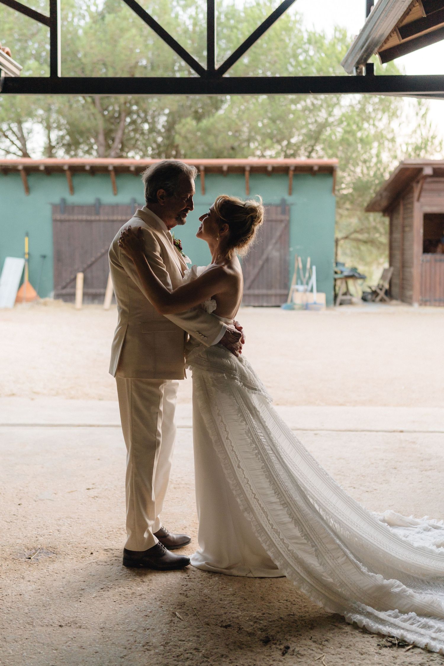 A couple shares an intimate moment under a rustic barn overhang.