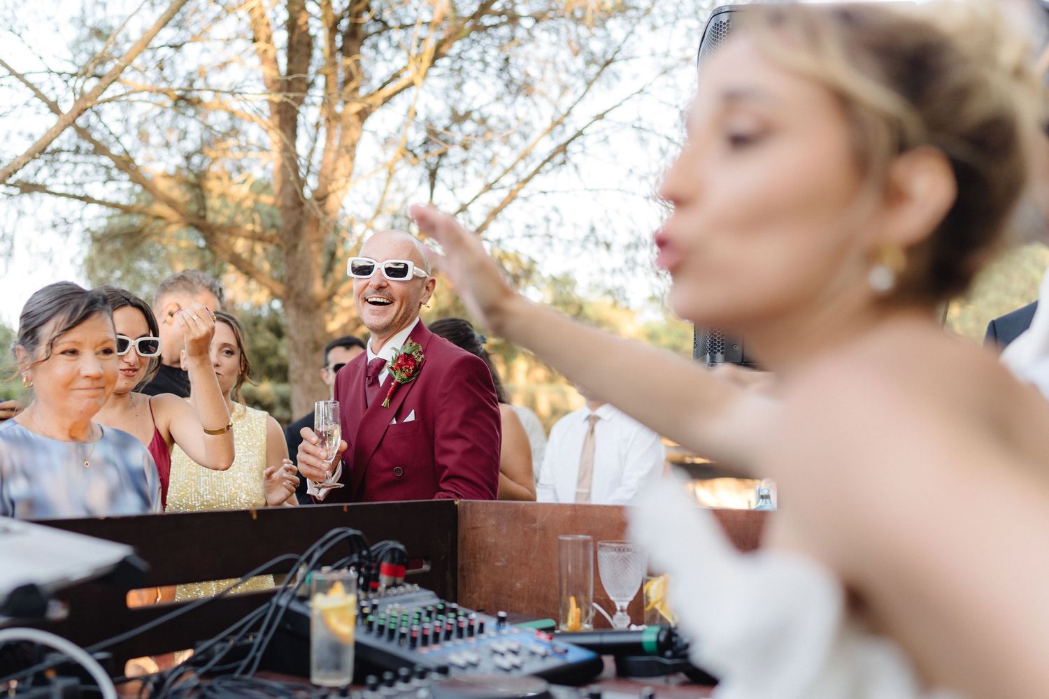 Wedding party dancing and celebrating with DJ equipment visible in outdoor setting.