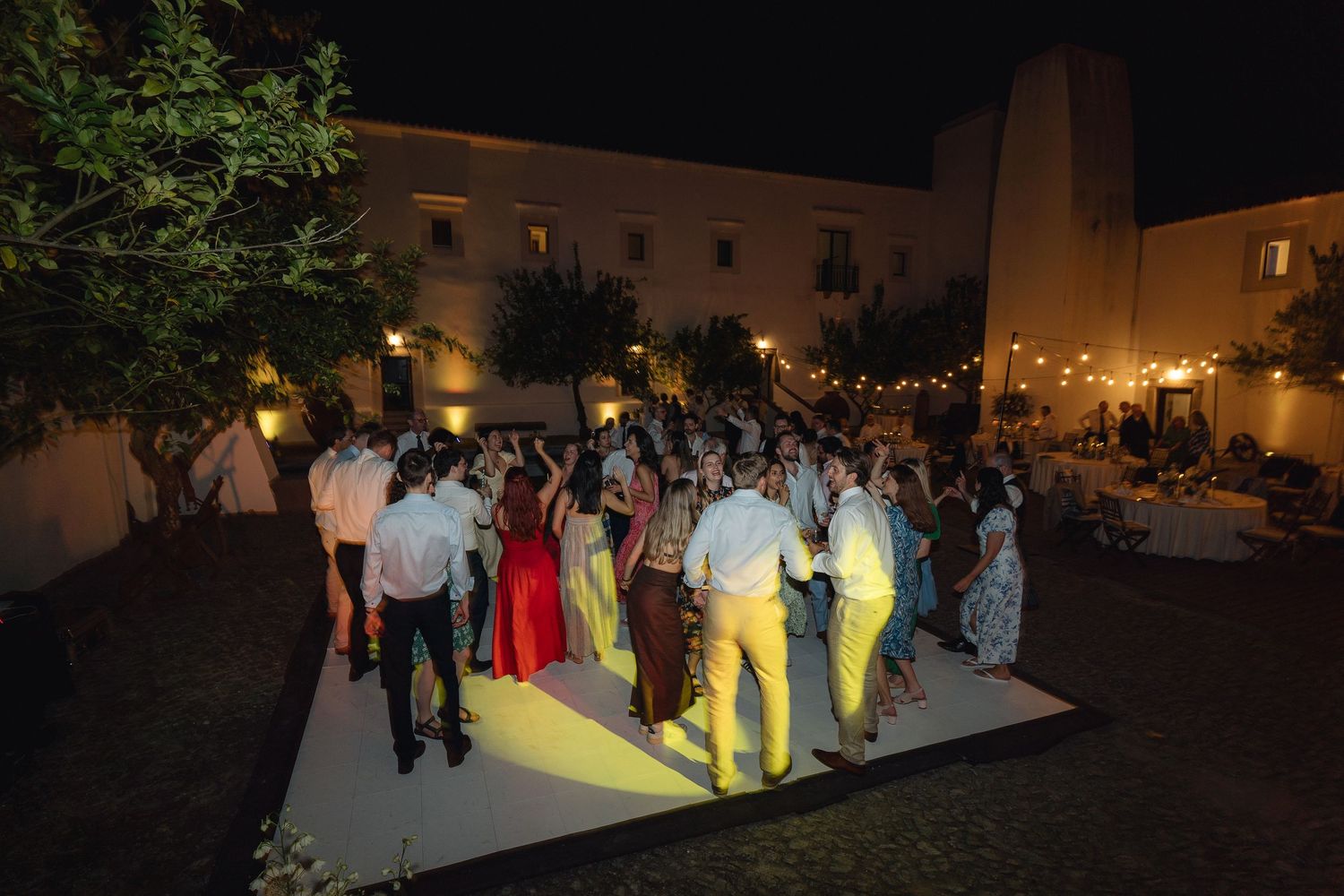 Illuminated outdoor dance floor with guests celebrating at a nighttime wedding reception.