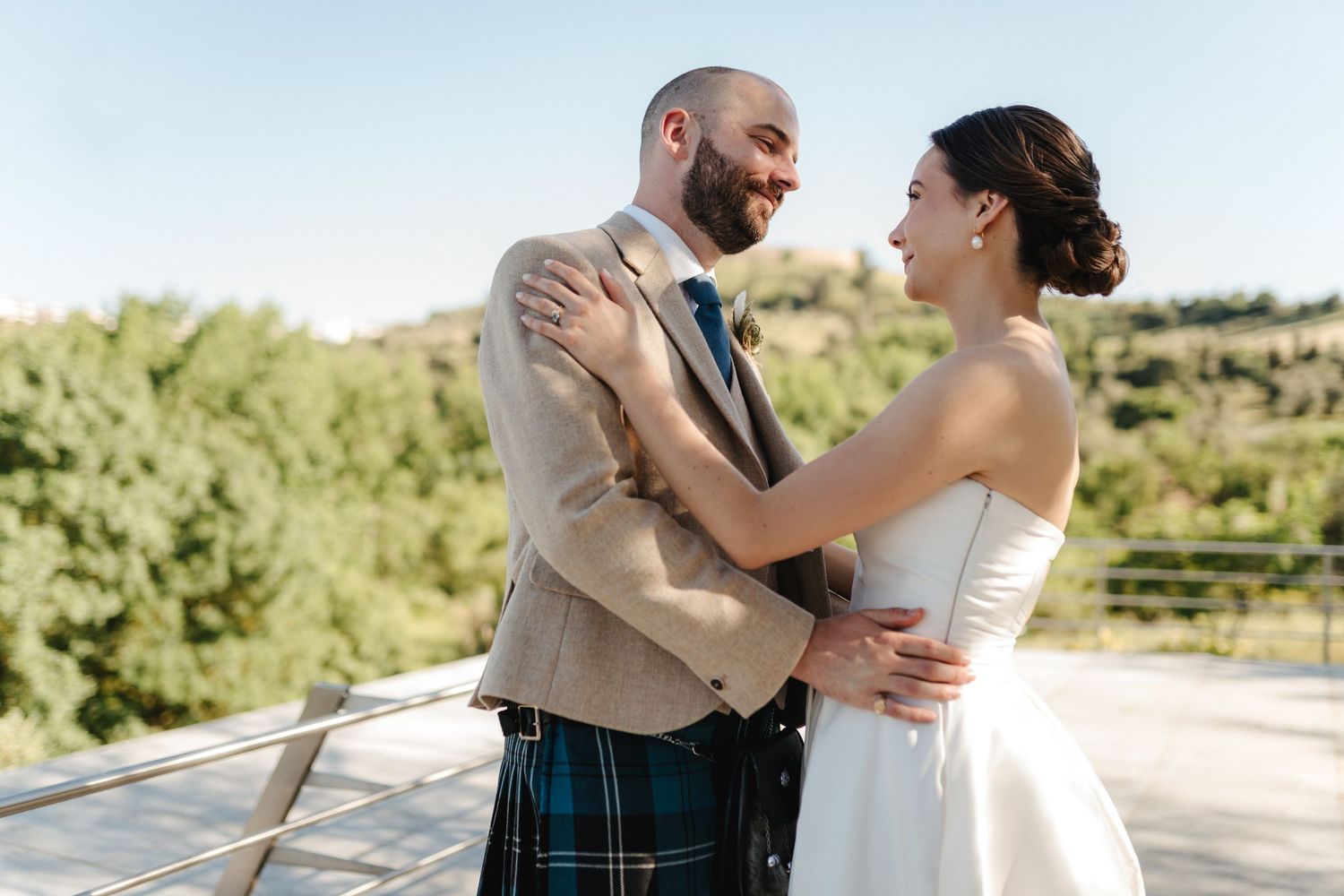 Newlyweds embrace against backdrop of rolling hills and blue sky.