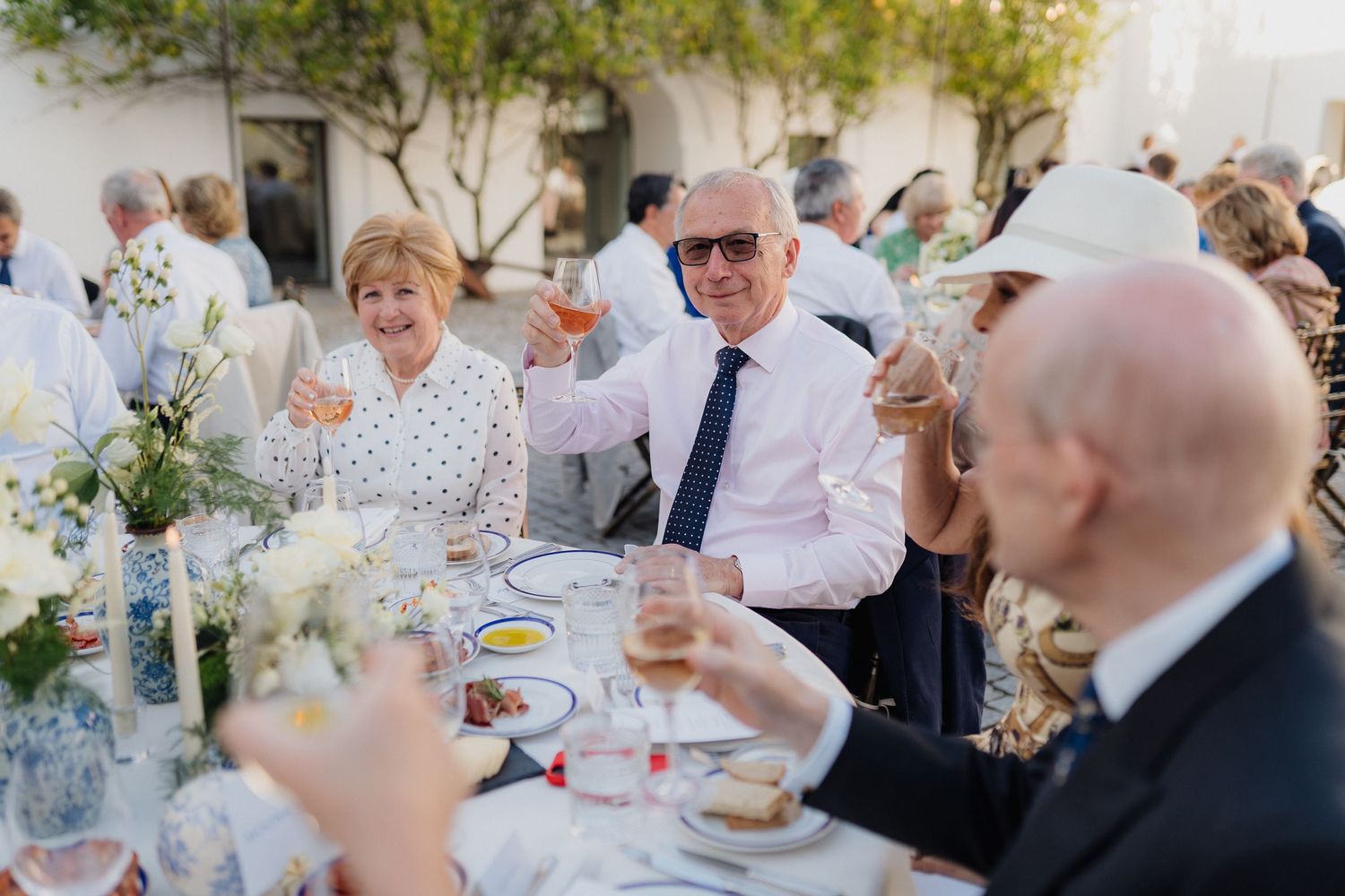 Guests enjoying wine and conversation at an elegant outdoor reception dinner with white table settings.