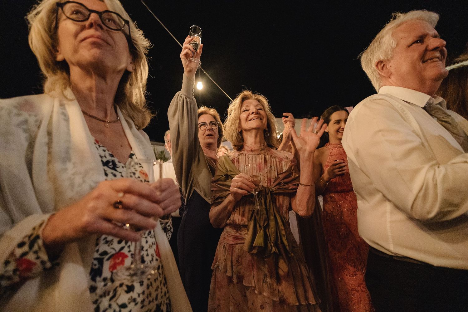 Wedding guests laugh and celebrate joyfully during an evening reception celebration.