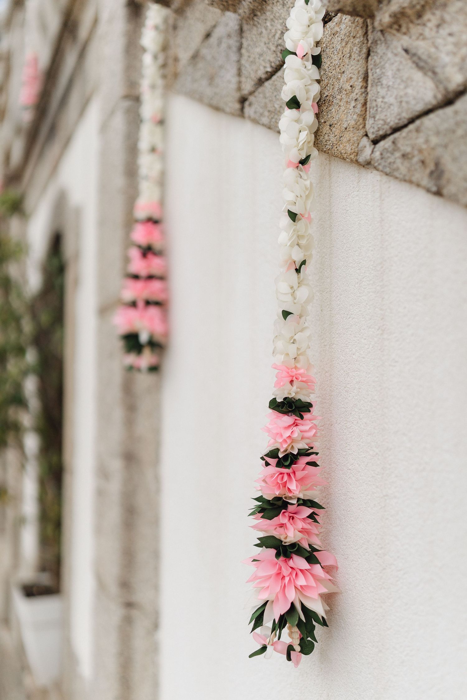 Pink and white floral garland hanging against a textured stone wall.