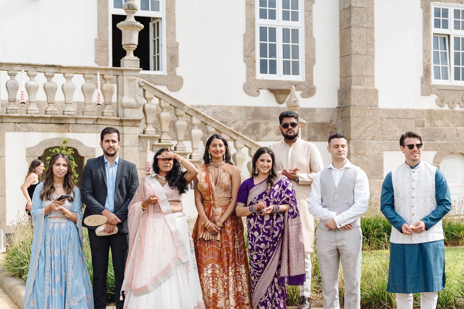 Wedding party group photo in front of elegant white stone building with classic architecture.