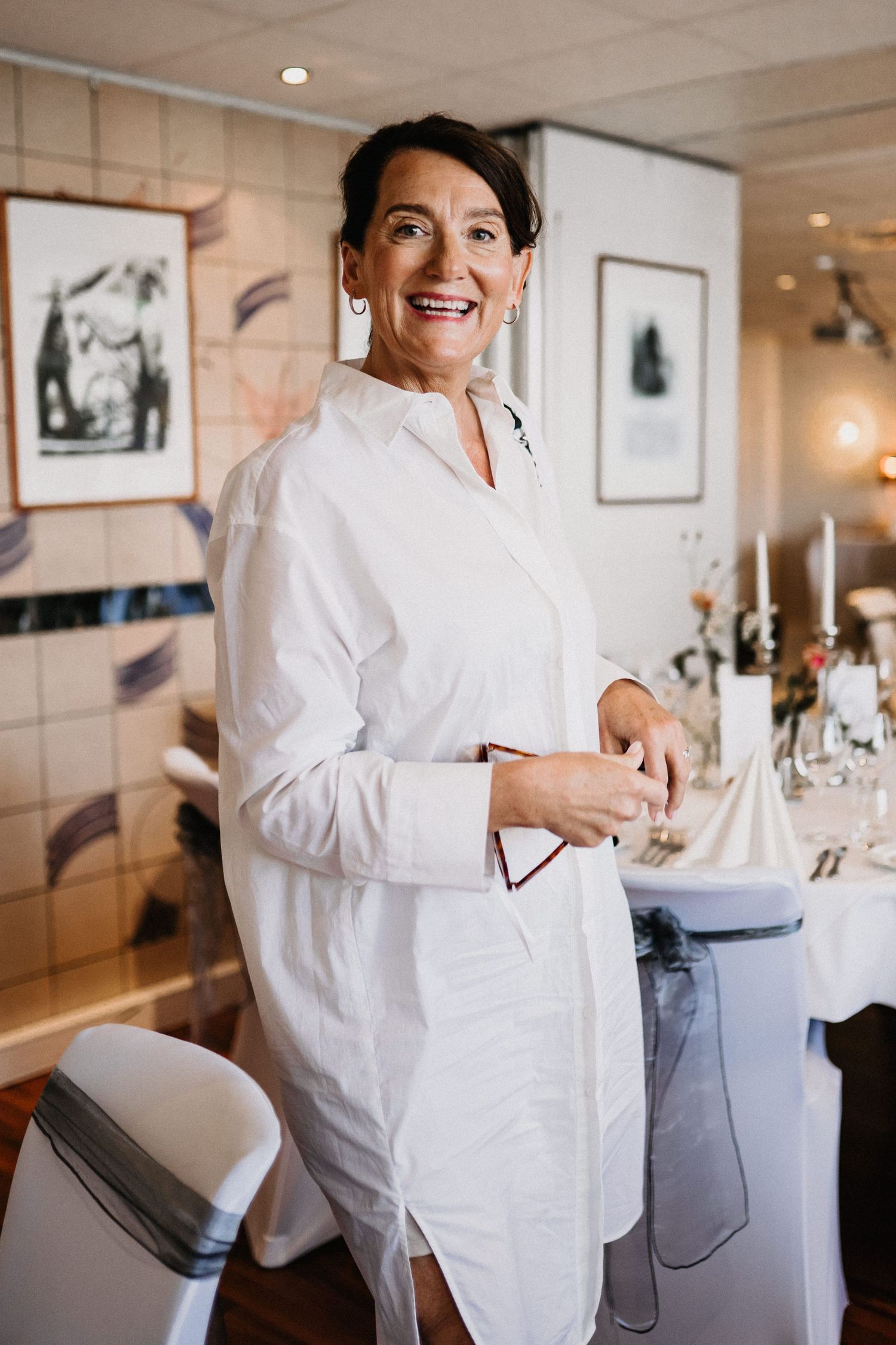 A white-robed figure moving through an elegant dining room with framed artwork and table settings.
