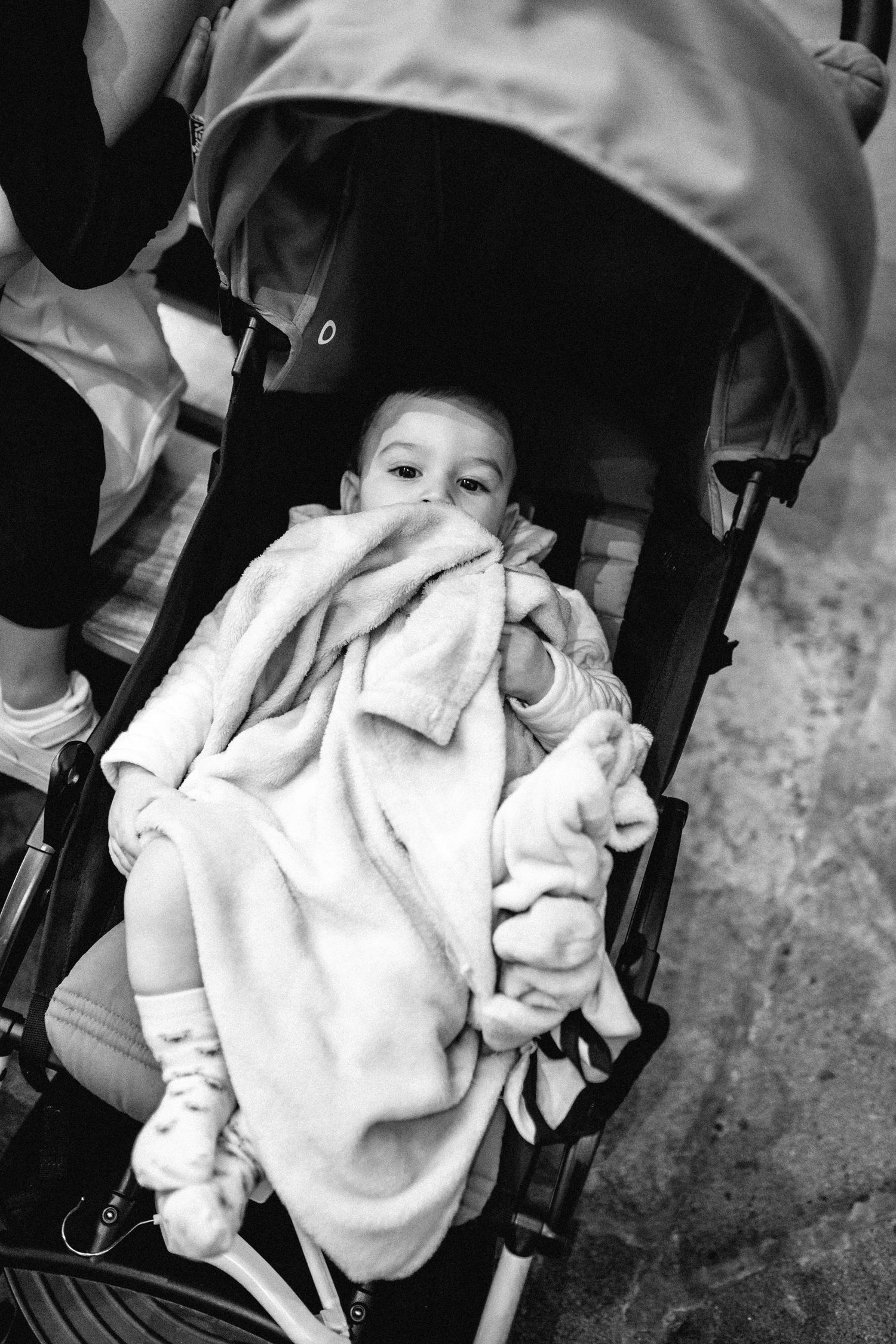 A small child bundled in a white blanket sits in a stroller.