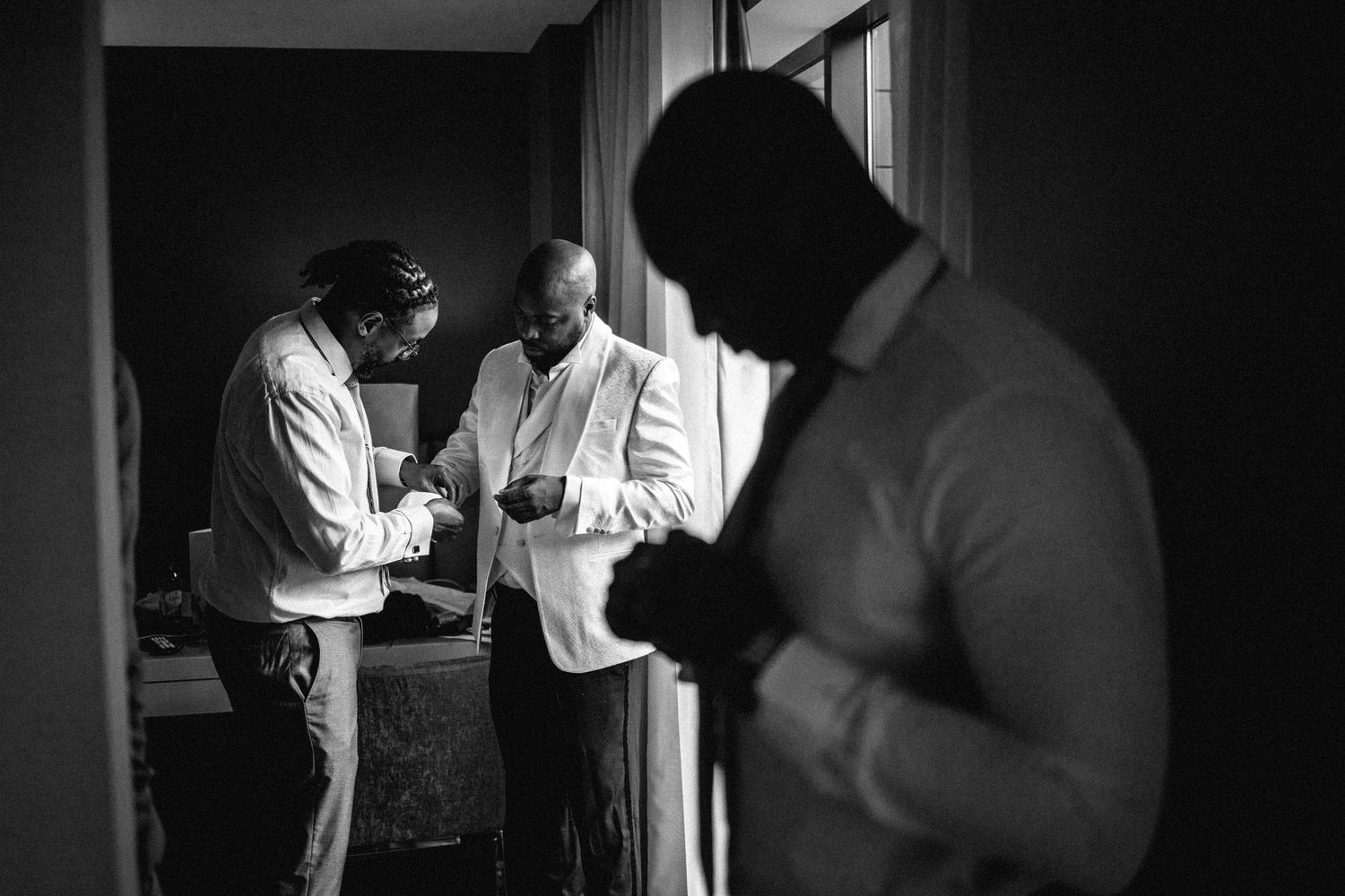 Black and white photo of groomsmen getting ready in a dimly lit room.