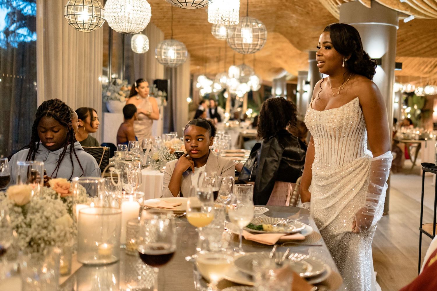 Wedding reception dinner features elegant table settings under crystal chandeliers.