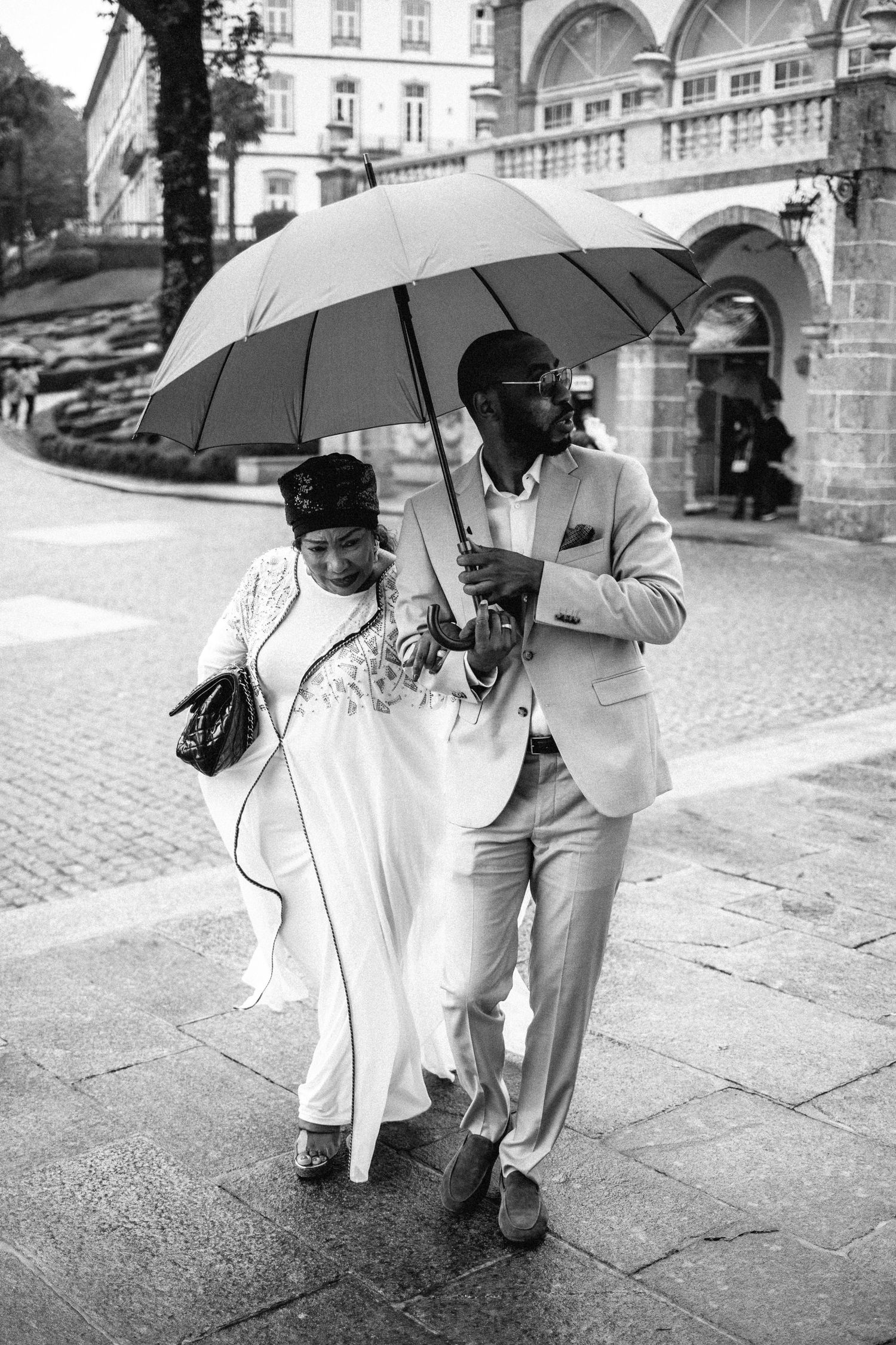 Black and white photos of people walking with umbrellas on a cobblestone street.