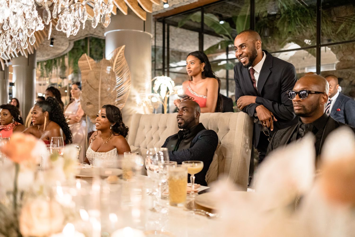 Wedding reception guests enjoying dinner and conversation under elegant chandeliers.