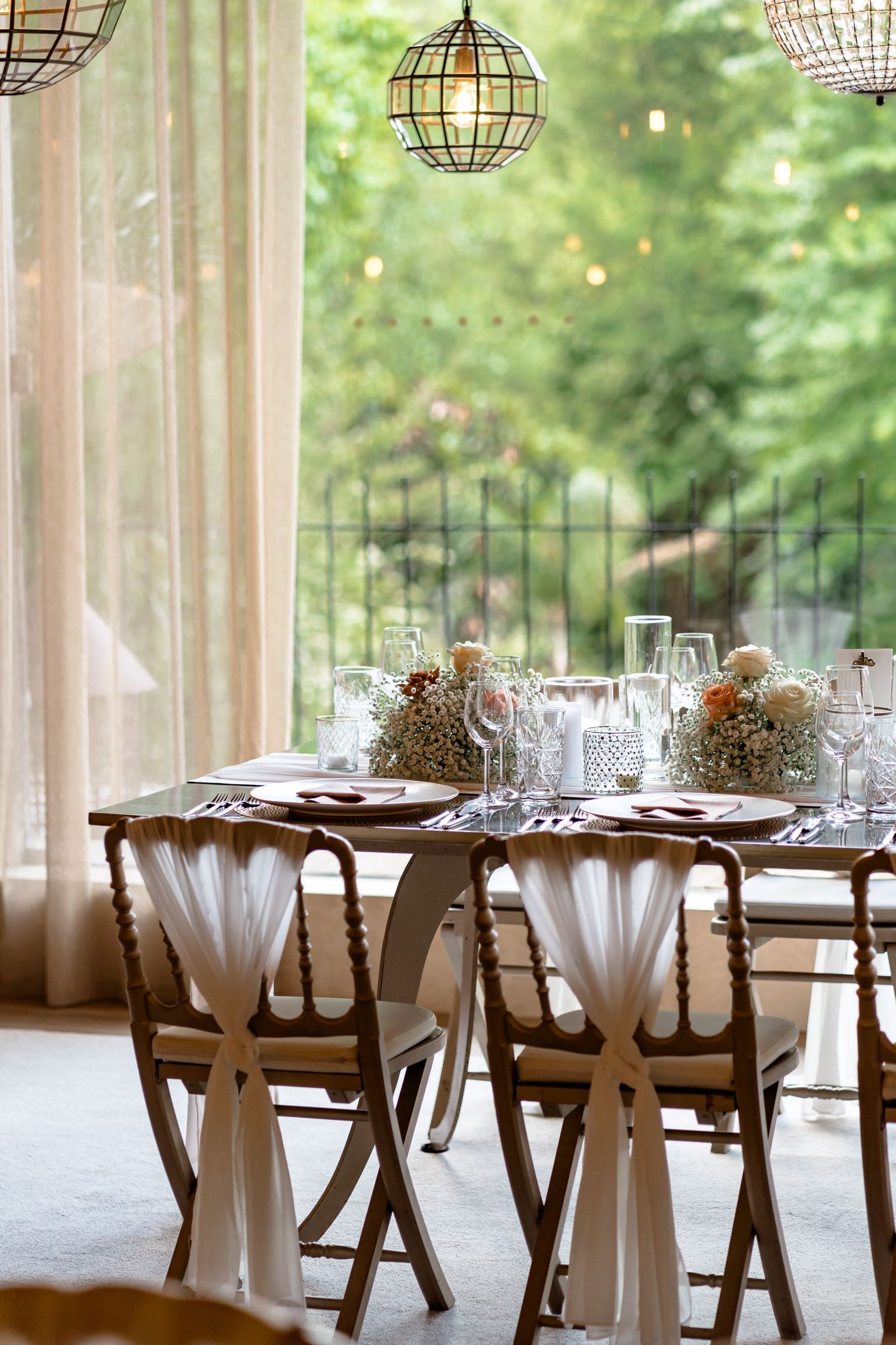 Romantic wedding reception table setup with draped chairs and hanging globe lights.