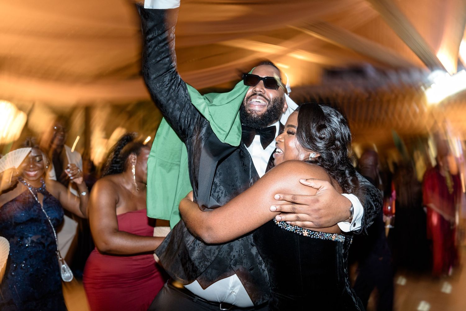 Guests dancing and celebrating at an indoor wedding reception with warm lighting.