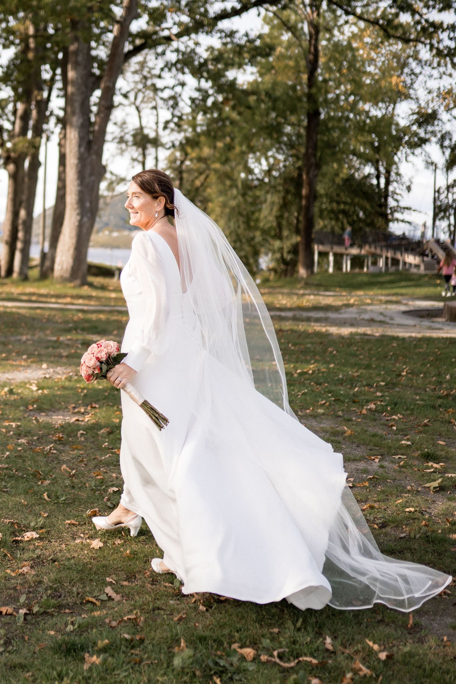 Flowing white wedding dress and veil captured in motion across an autumn park setting.