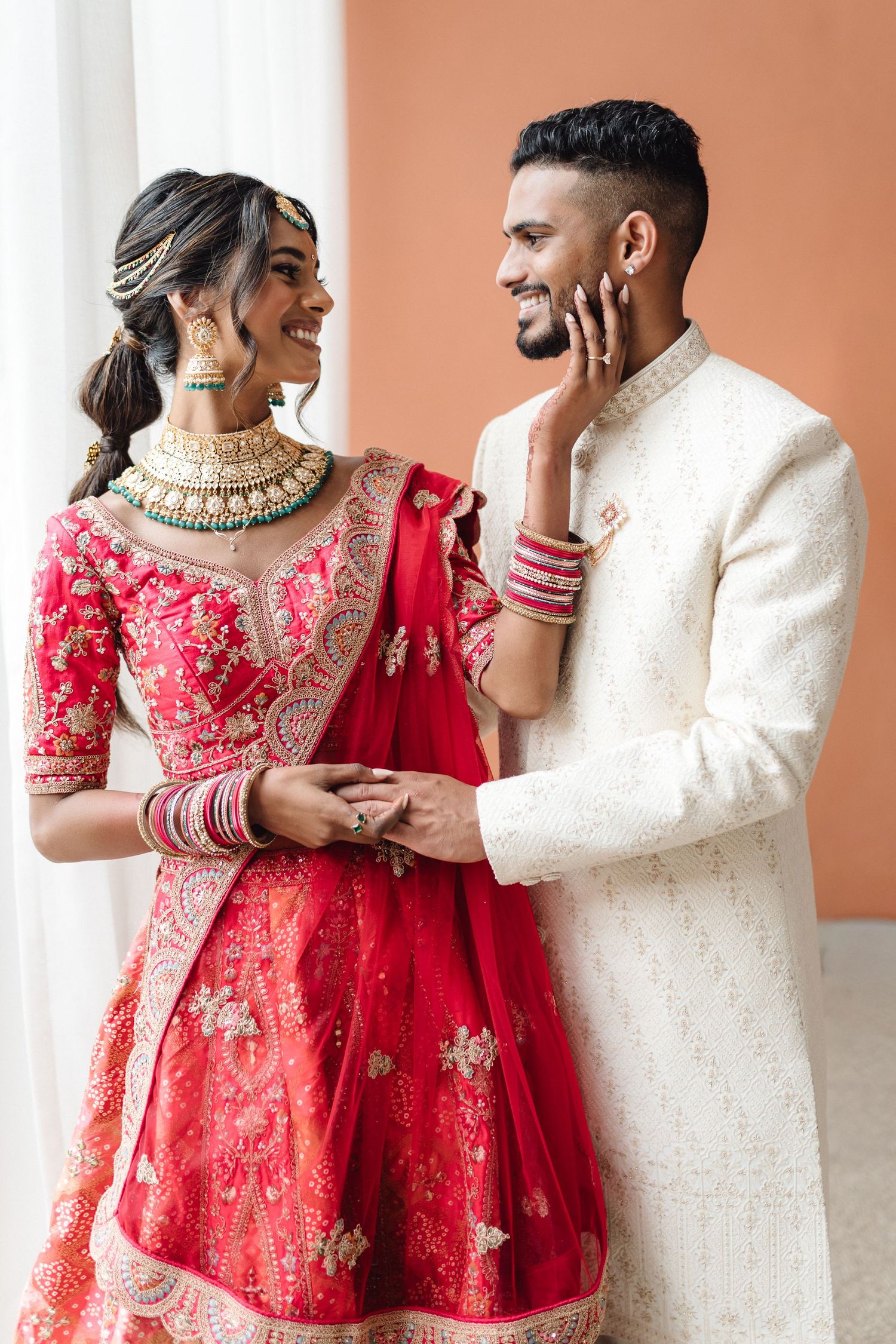 Traditional Indian wedding attire featuring red lehenga with gold embroidery and white sherwani.