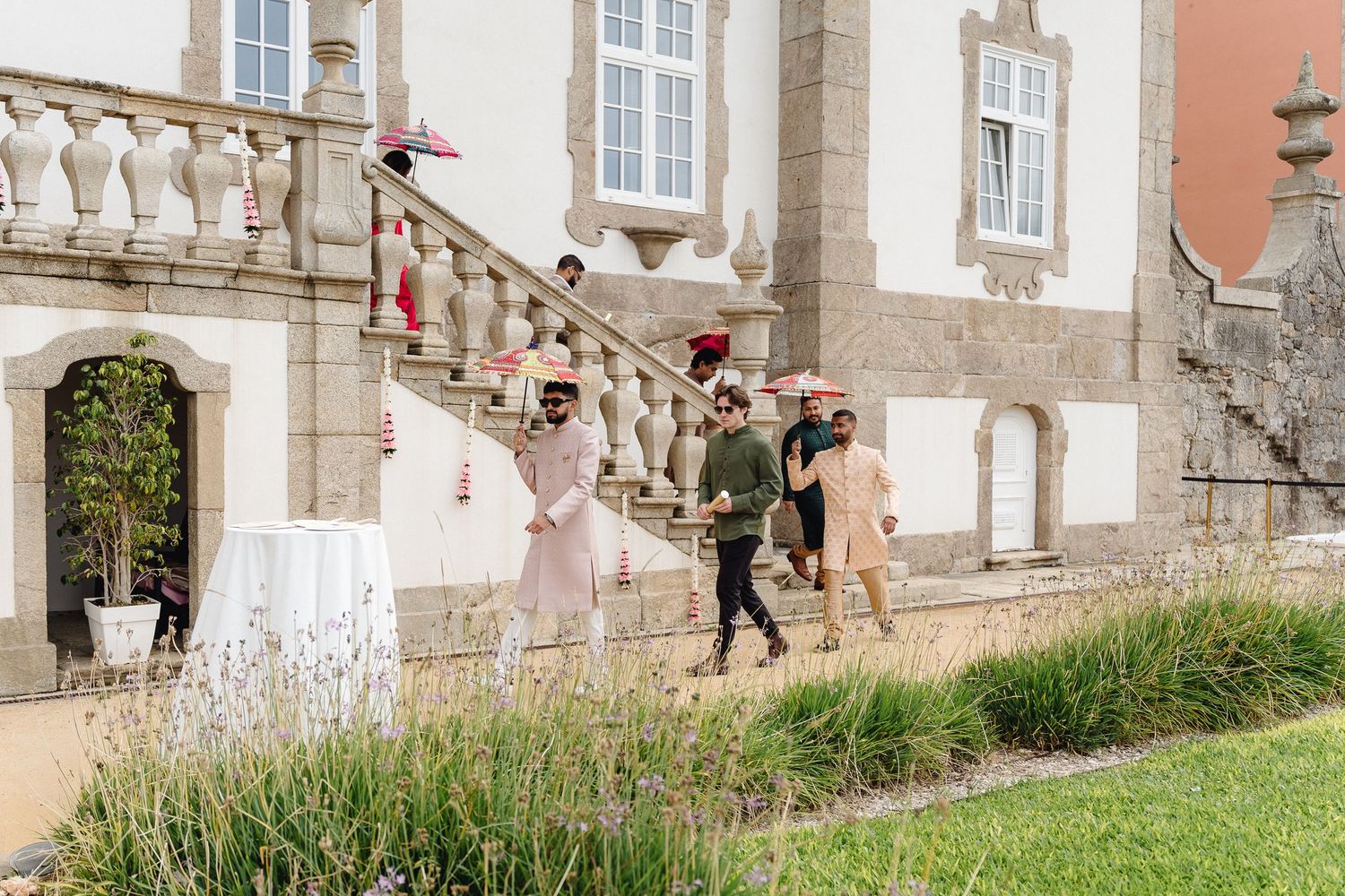 Stone building exterior with grass lawn and people walking along the balustrade.