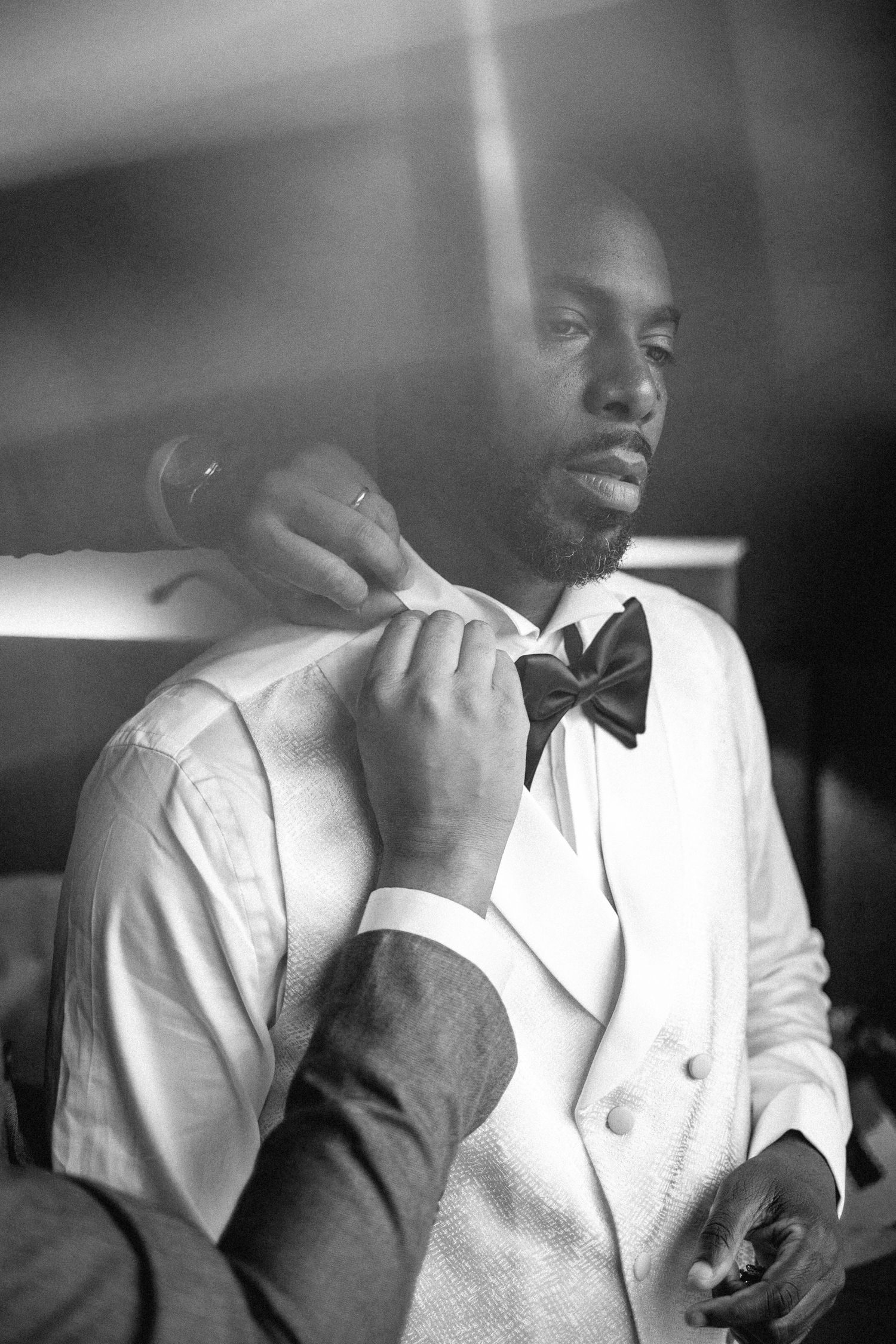 A close-up black and white portrait of someone adjusting their bowtie.