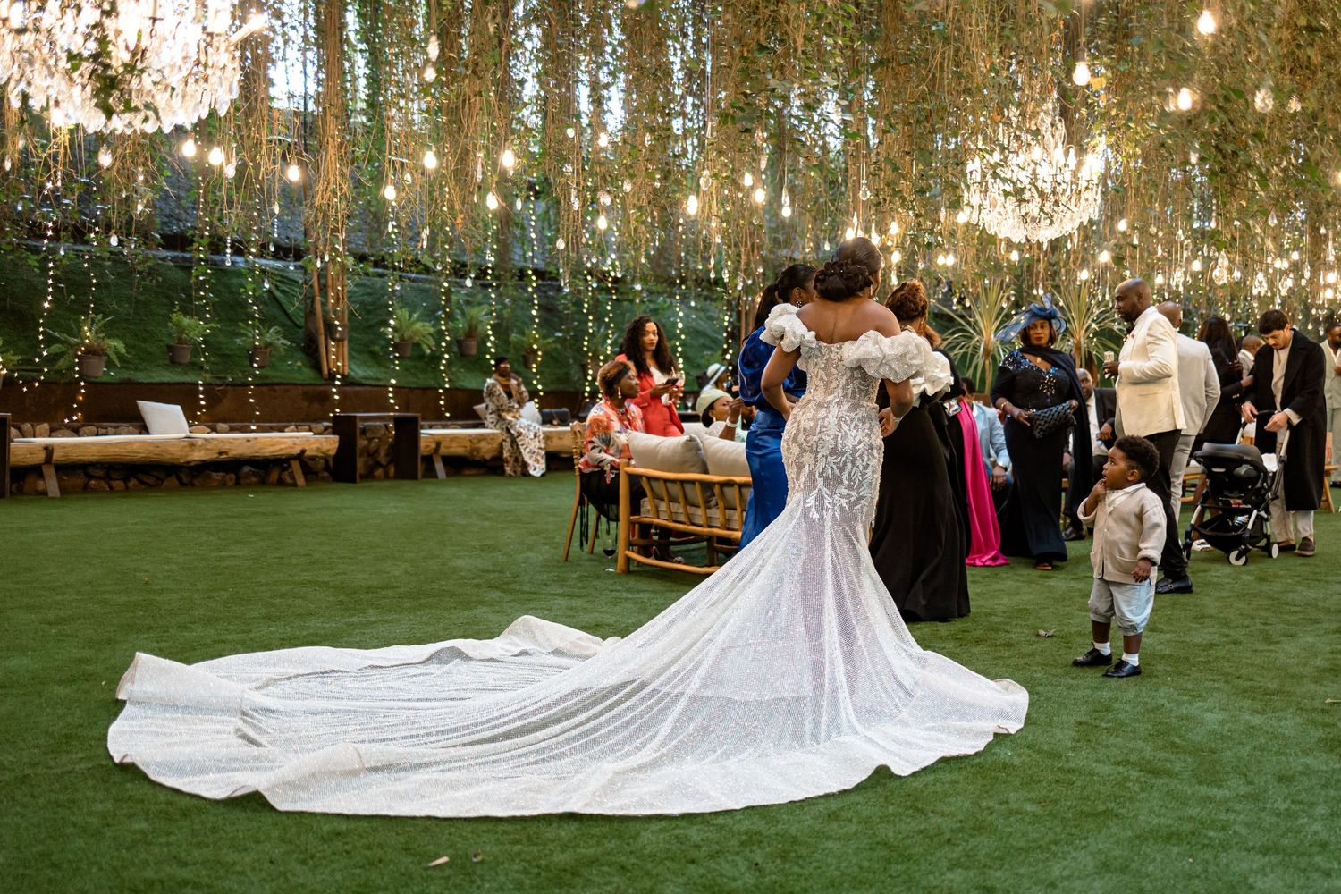 Outdoor wedding reception under hanging string lights with a flowing white wedding dress train.
