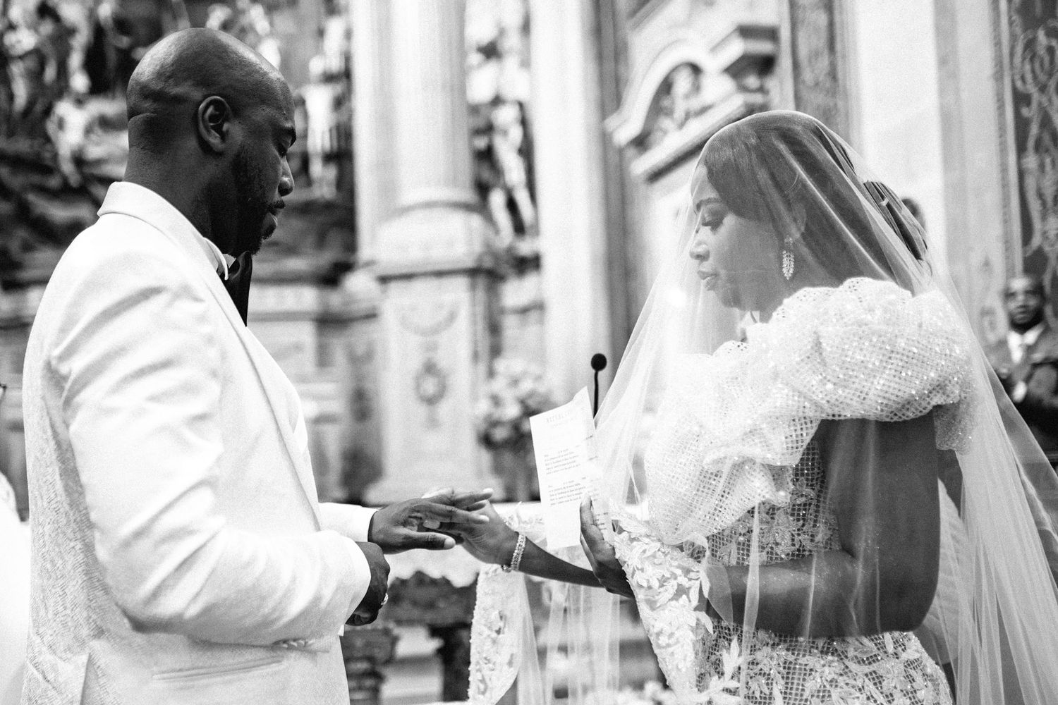 A couple exchanges rings during their wedding ceremony in an ornate church setting.