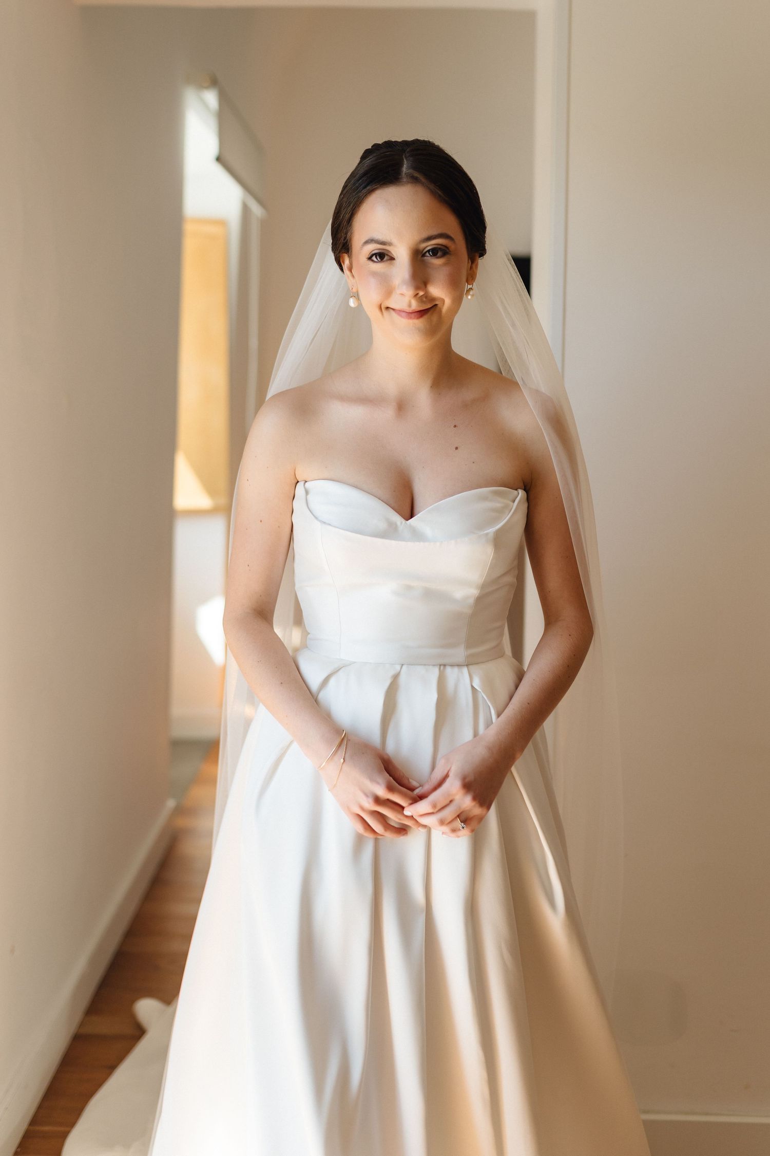 Elegant bride poses in simple white wedding gown and flowing veil.