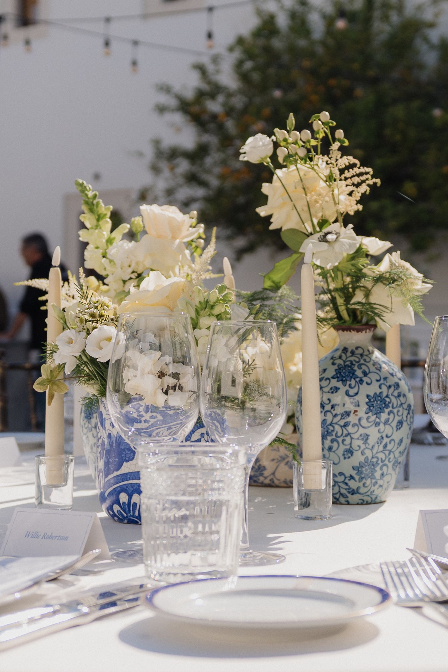 Elegant table setting with blue and white chinoiserie vases filled with white flowers and crystal glassware.