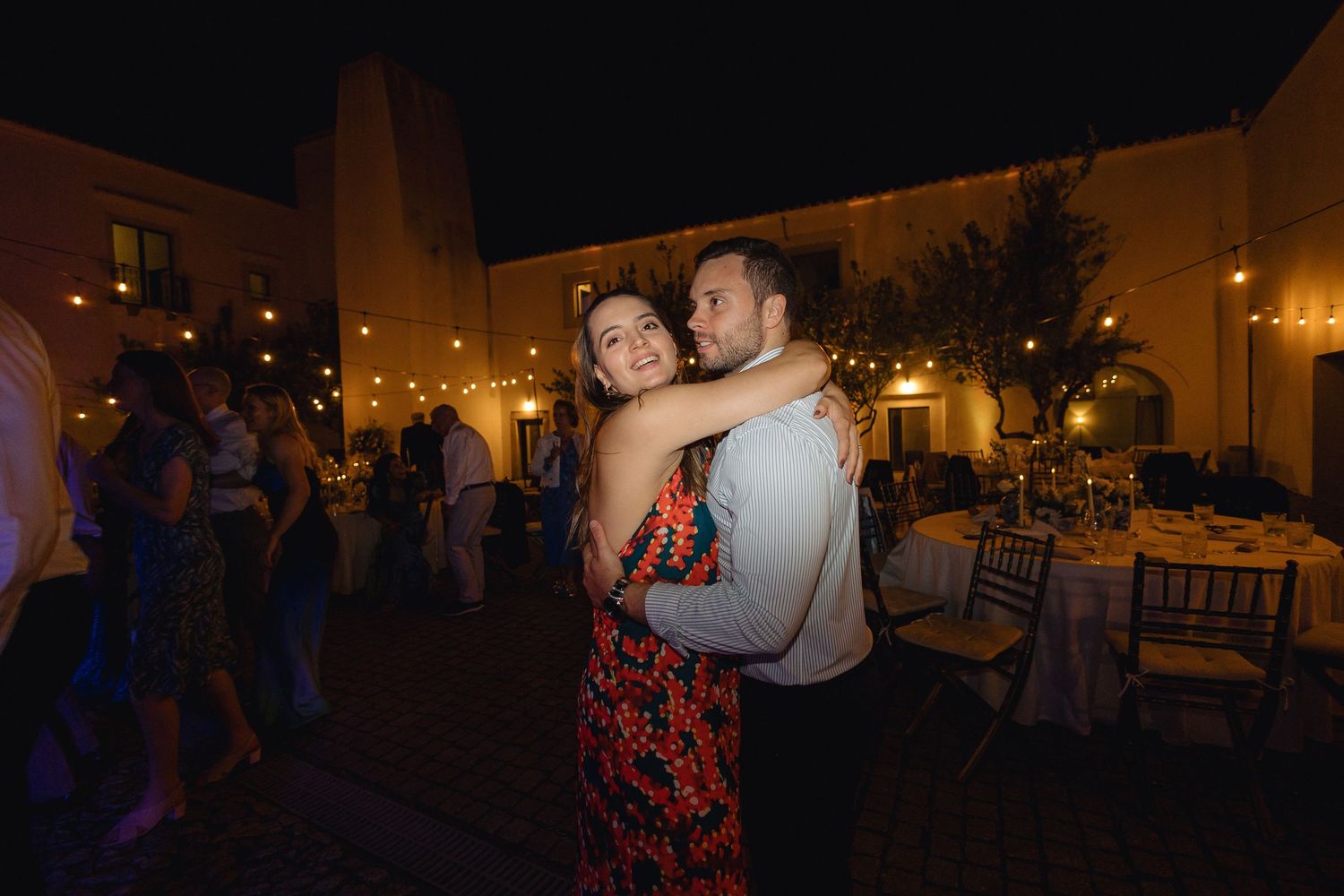 Panoramic view of an outdoor evening wedding reception with ambient lighting.
