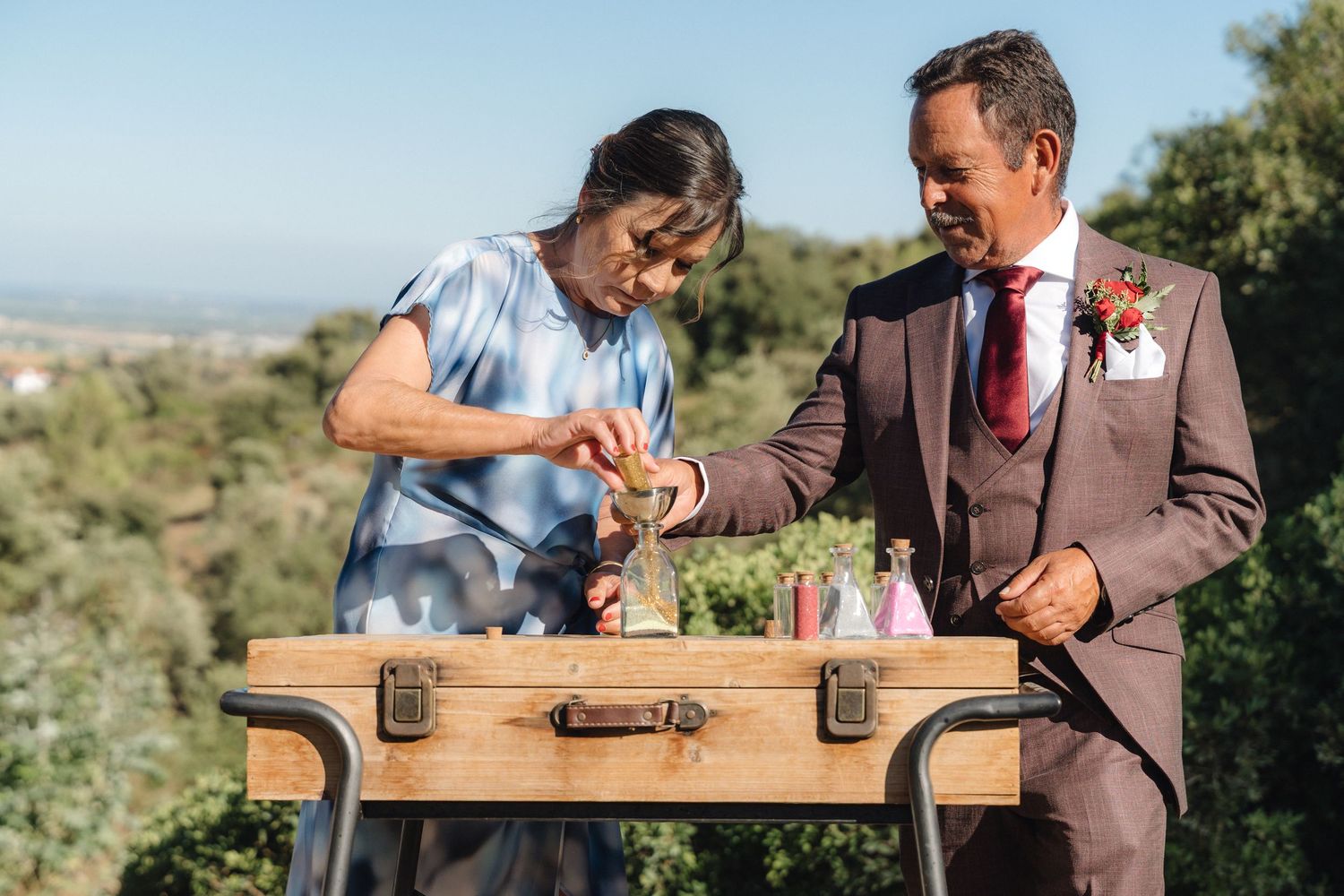 Wedding party members interact playfully with a wooden chest outdoors.