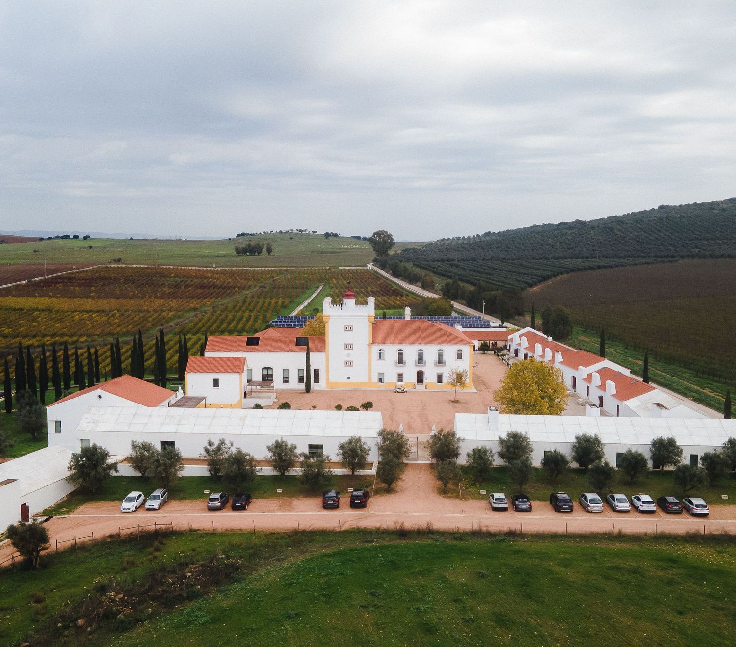Panoramic view of a white Mediterranean-style estate with parking area surrounded by rolling hills.