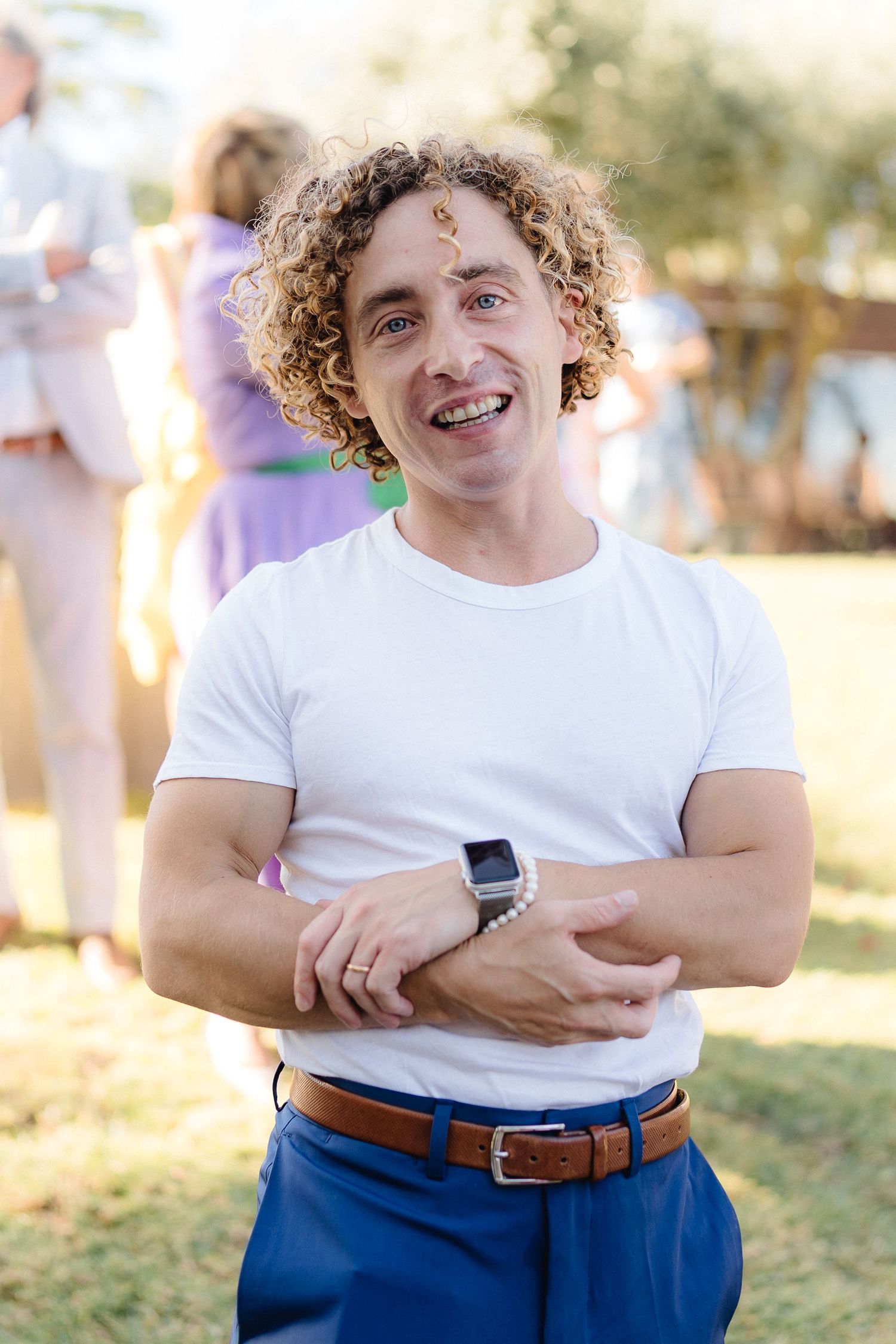 Person in white t-shirt and blue pants smiles warmly at outdoor event.