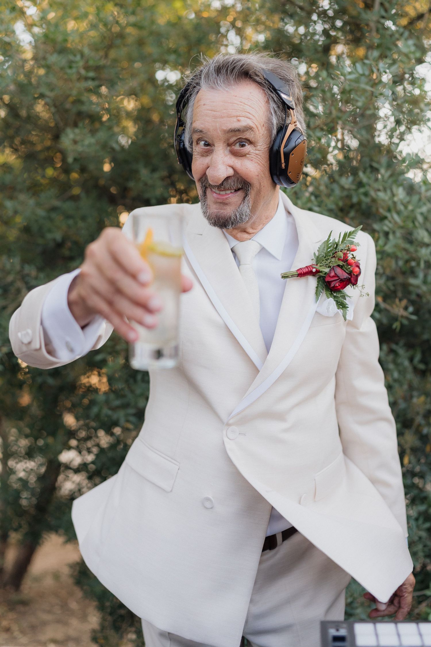 DJ in white suit and red boutonniere performing animated set at outdoor wedding.