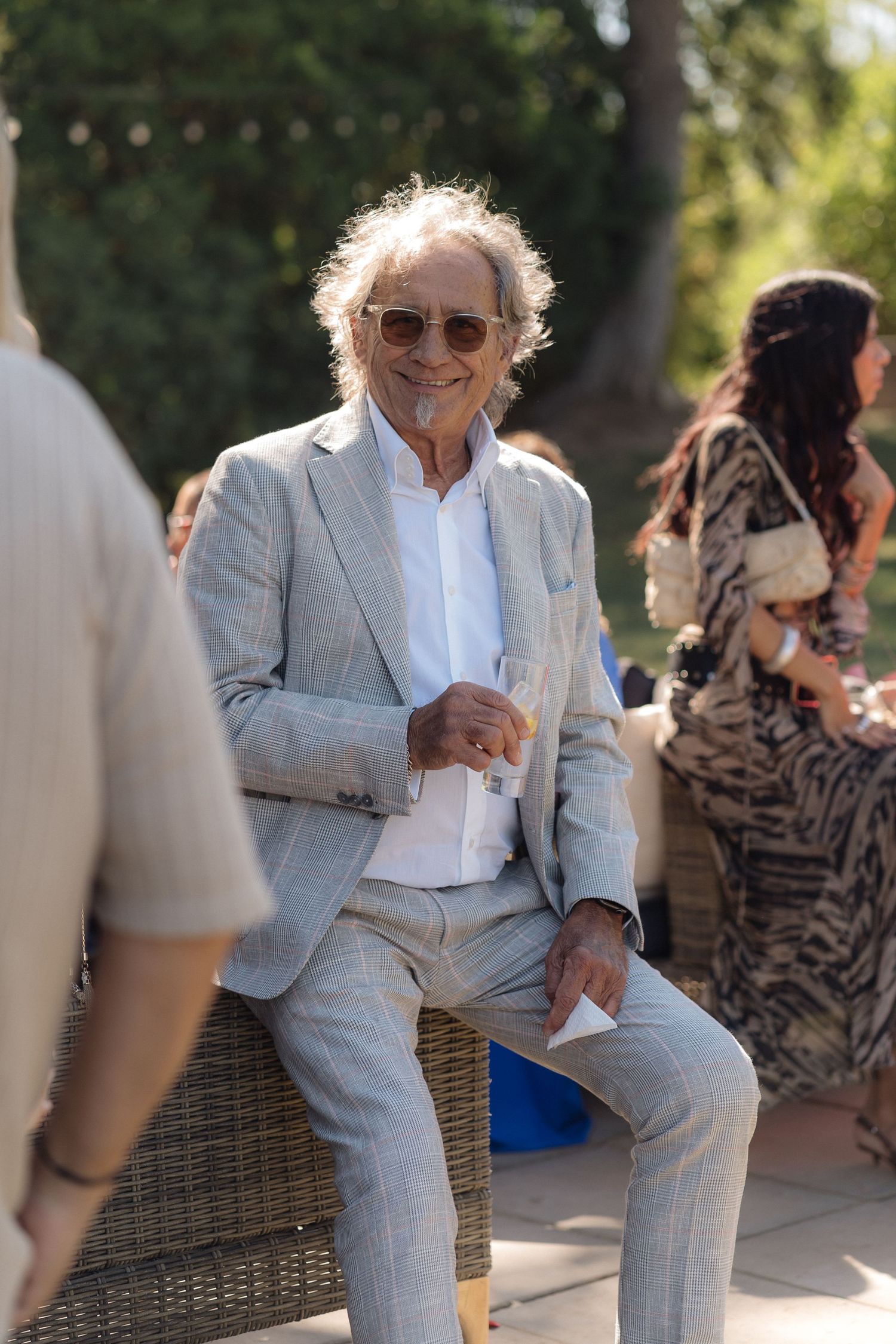 Person in light gray suit sitting casually on wicker furniture at outdoor event.
