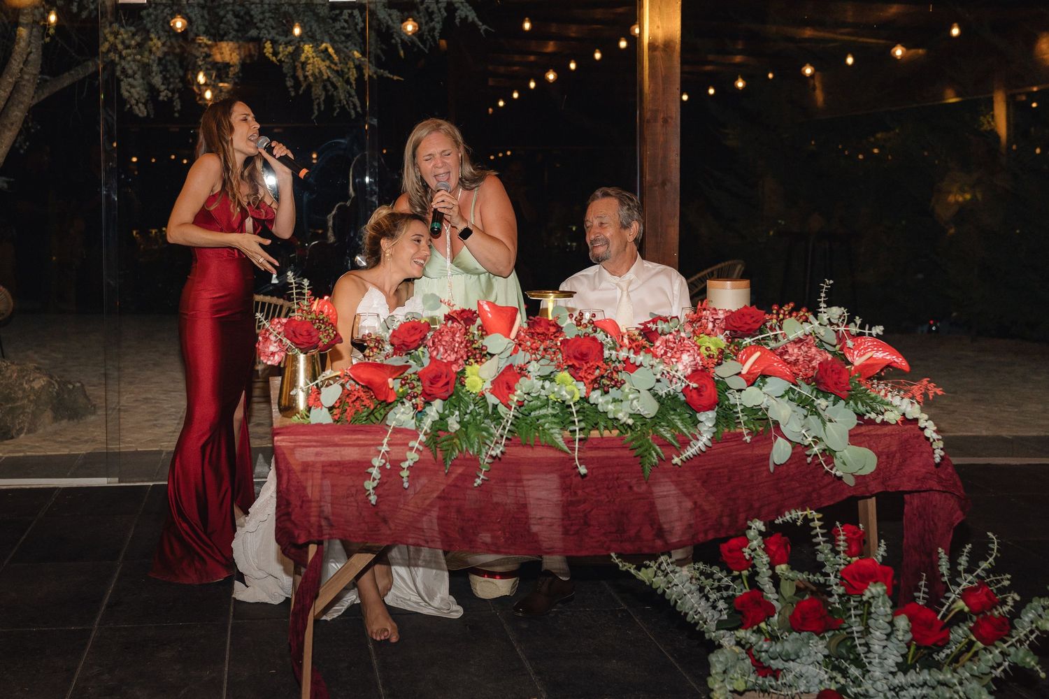 Elegant table decorations with red roses and greenery at an evening wedding reception.