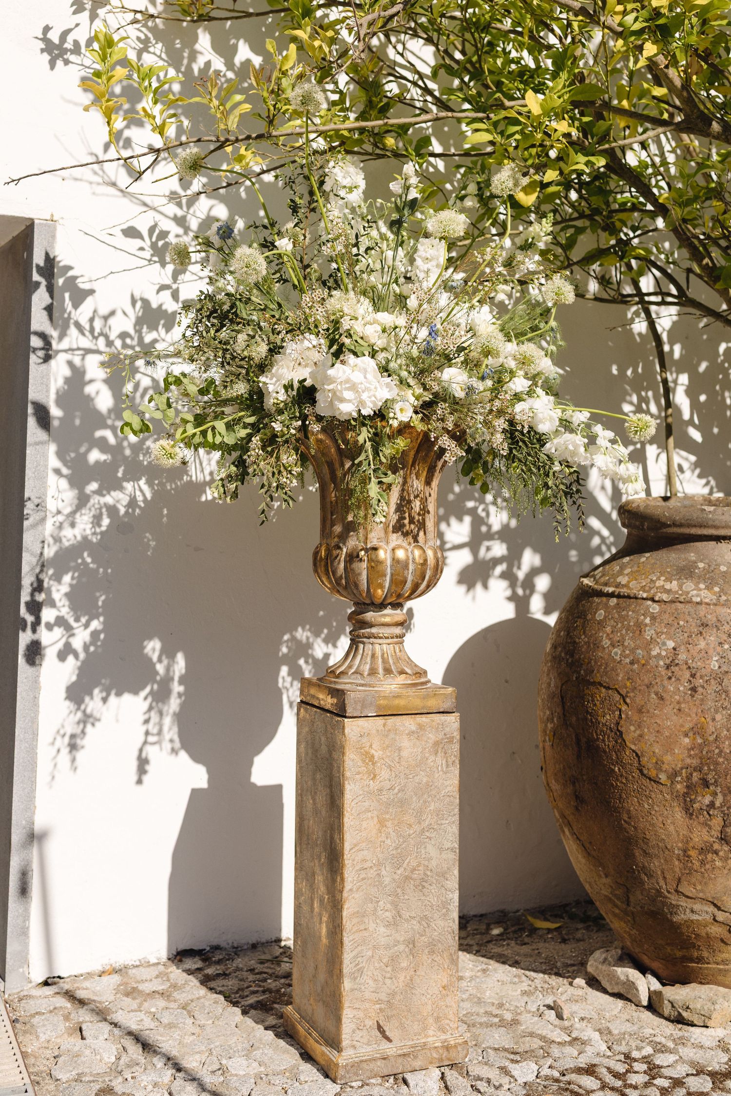 Rustic stone urns and planters with greenery against a white wall in Mediterranean style.