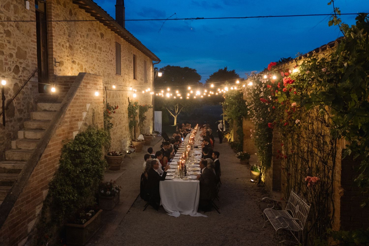 Elegant outdoor dinner party at dusk with string lights at a rustic Tuscan villa.